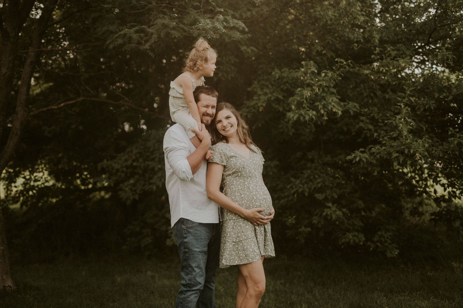 A couple shares an intimate embrace outdoors during a romantic photoshoot in a wooded natural setting.