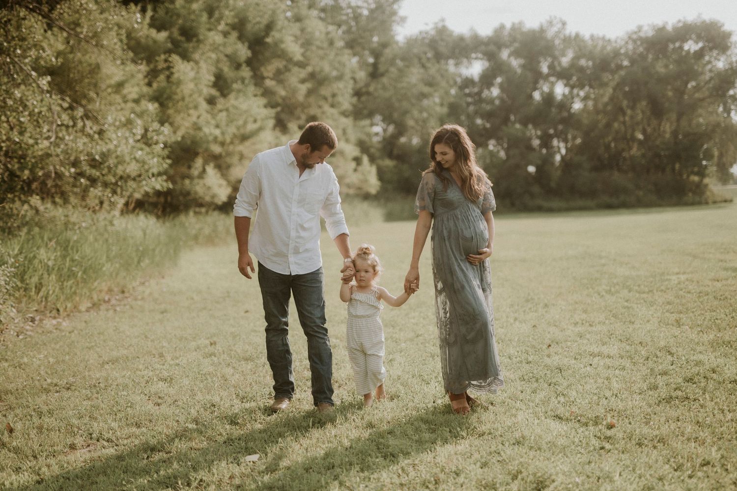 Family enjoying a candid outdoor photo session in a sunlit meadow with natural muted tones.