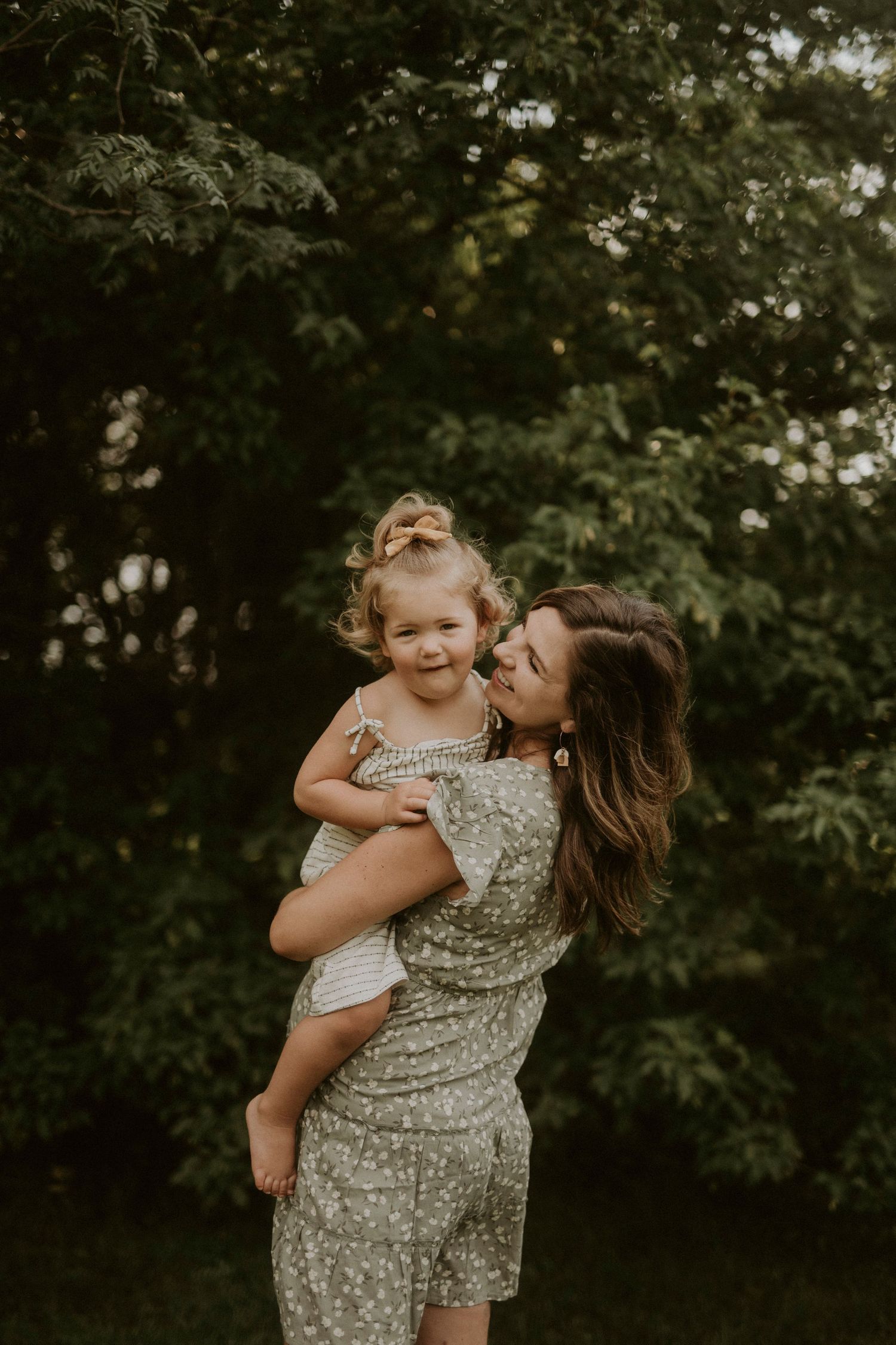 A tender moment captured outdoors as parent and child share joyful laughter against a leafy green background.