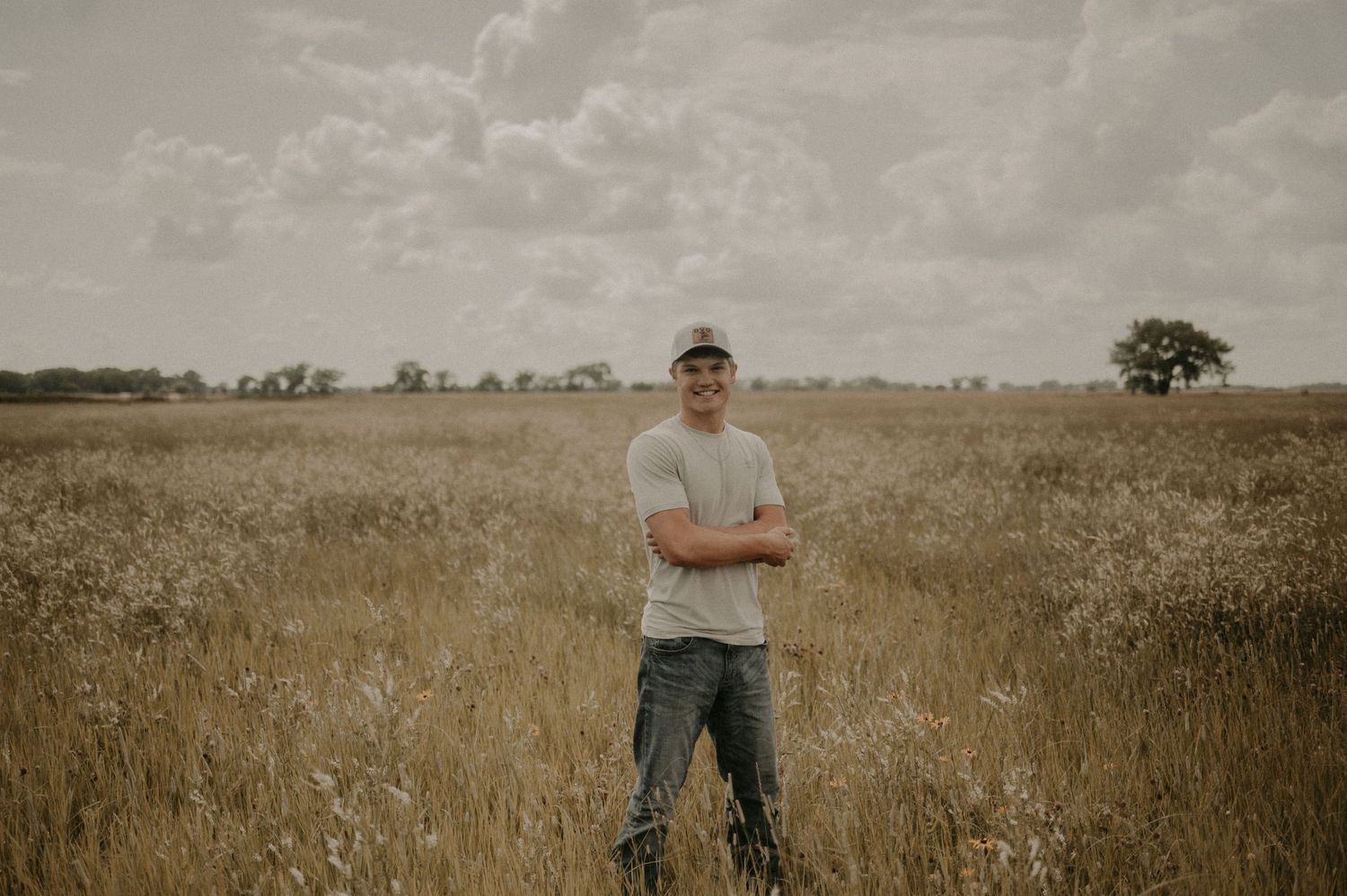 Person standing in a golden wheat field under cloudy skies during harvest season.