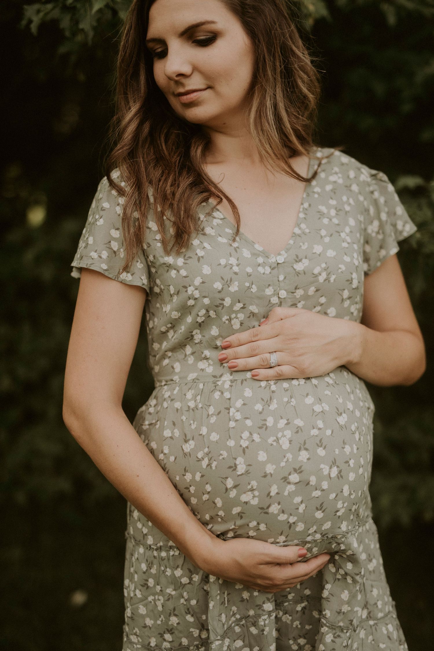 A person in a sage green floral dress touches their pregnant belly in a series of intimate maternity photos.