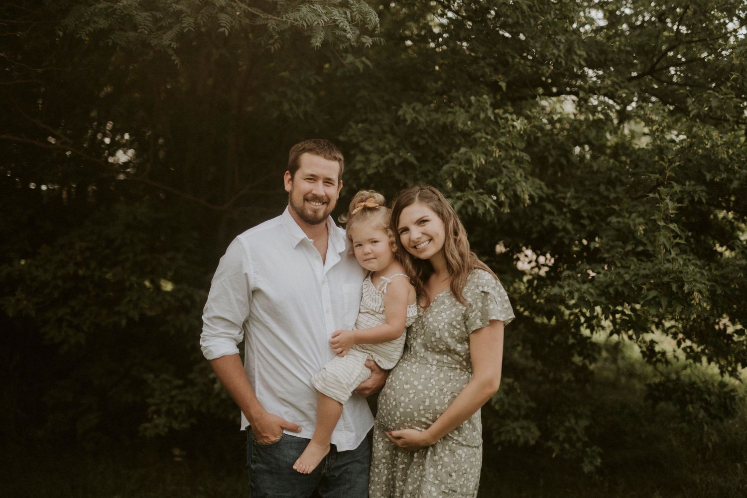 A family shares tender moments together in a lush green outdoor setting during a professional photo session.