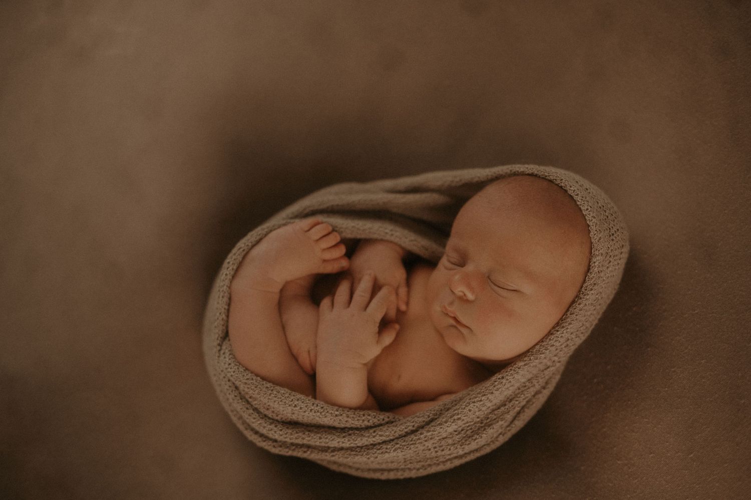 A series of sepia-toned photos showing a sleeping newborn baby wrapped in soft knit blankets.
