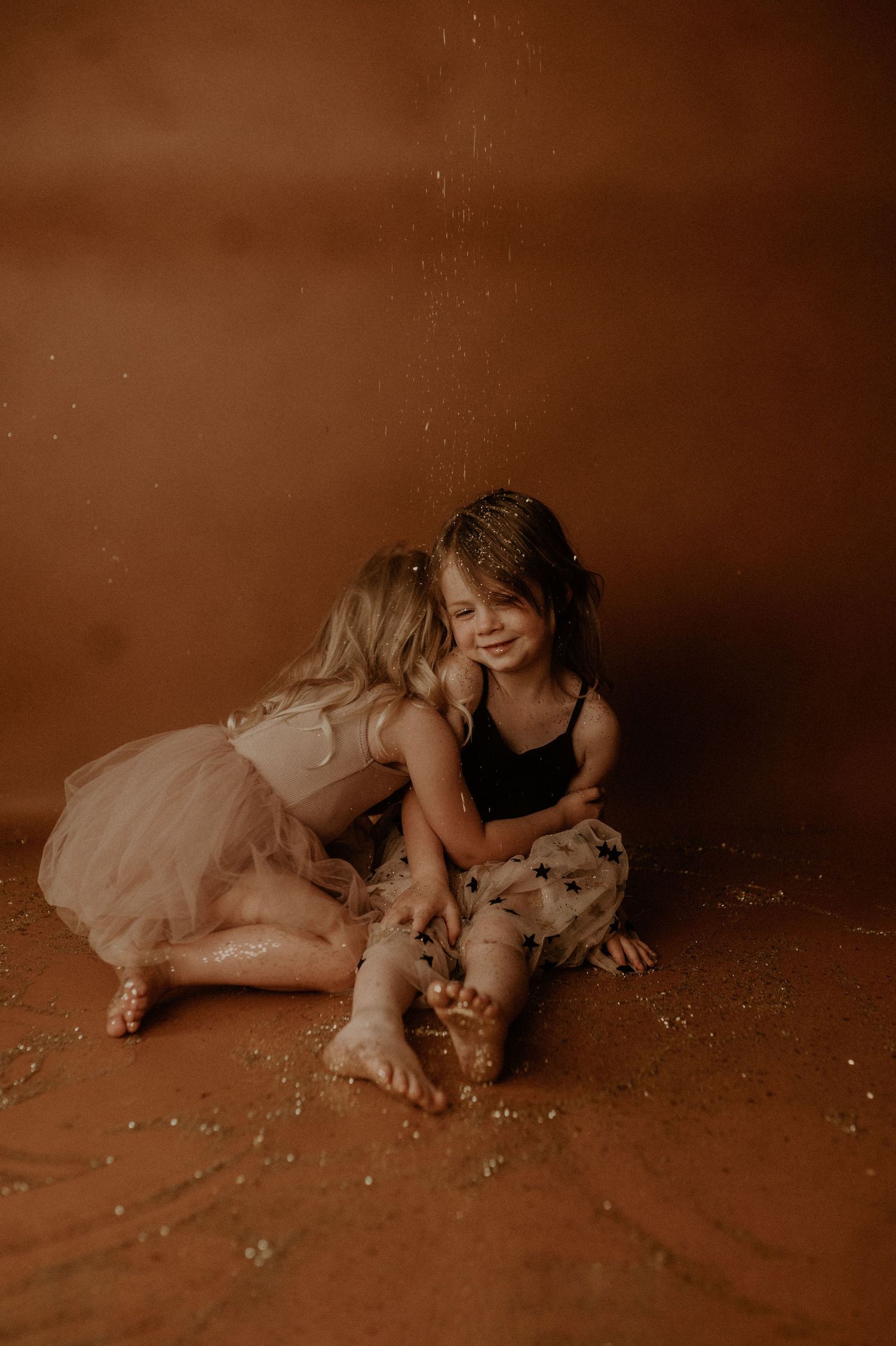 A child in a tulle dress lies on a brown floor in a series of artistic sepia-toned photographs.
