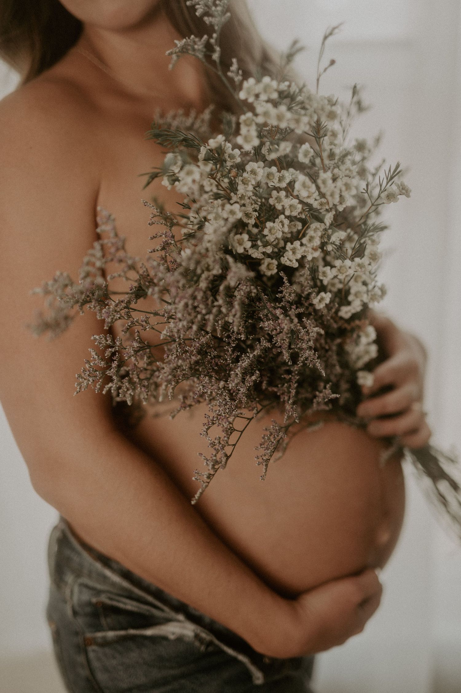 Intimate maternity photo with dried flowers held against bare belly.