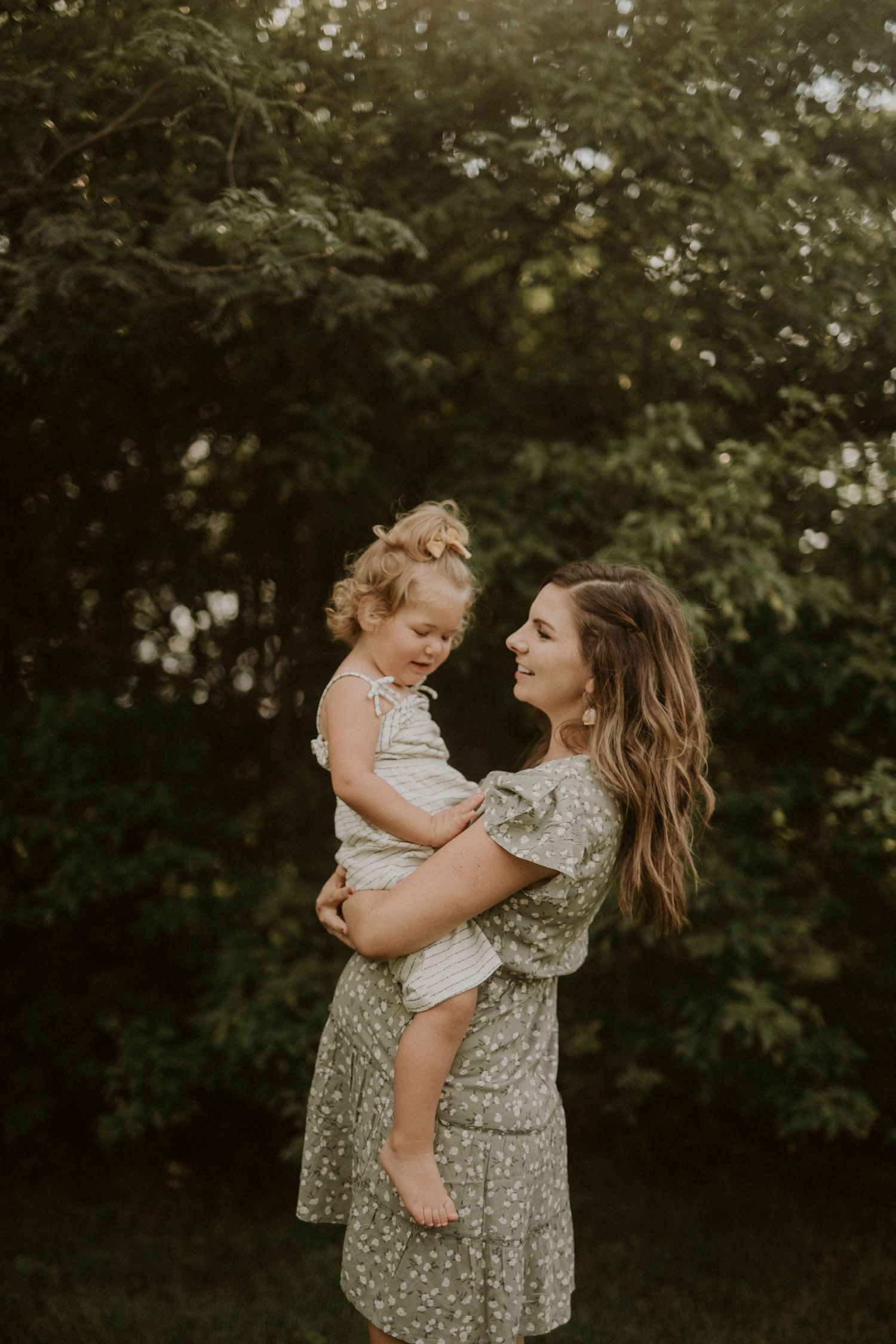 A mother and child share tender moments in a series of outdoor portraits against a lush green background.