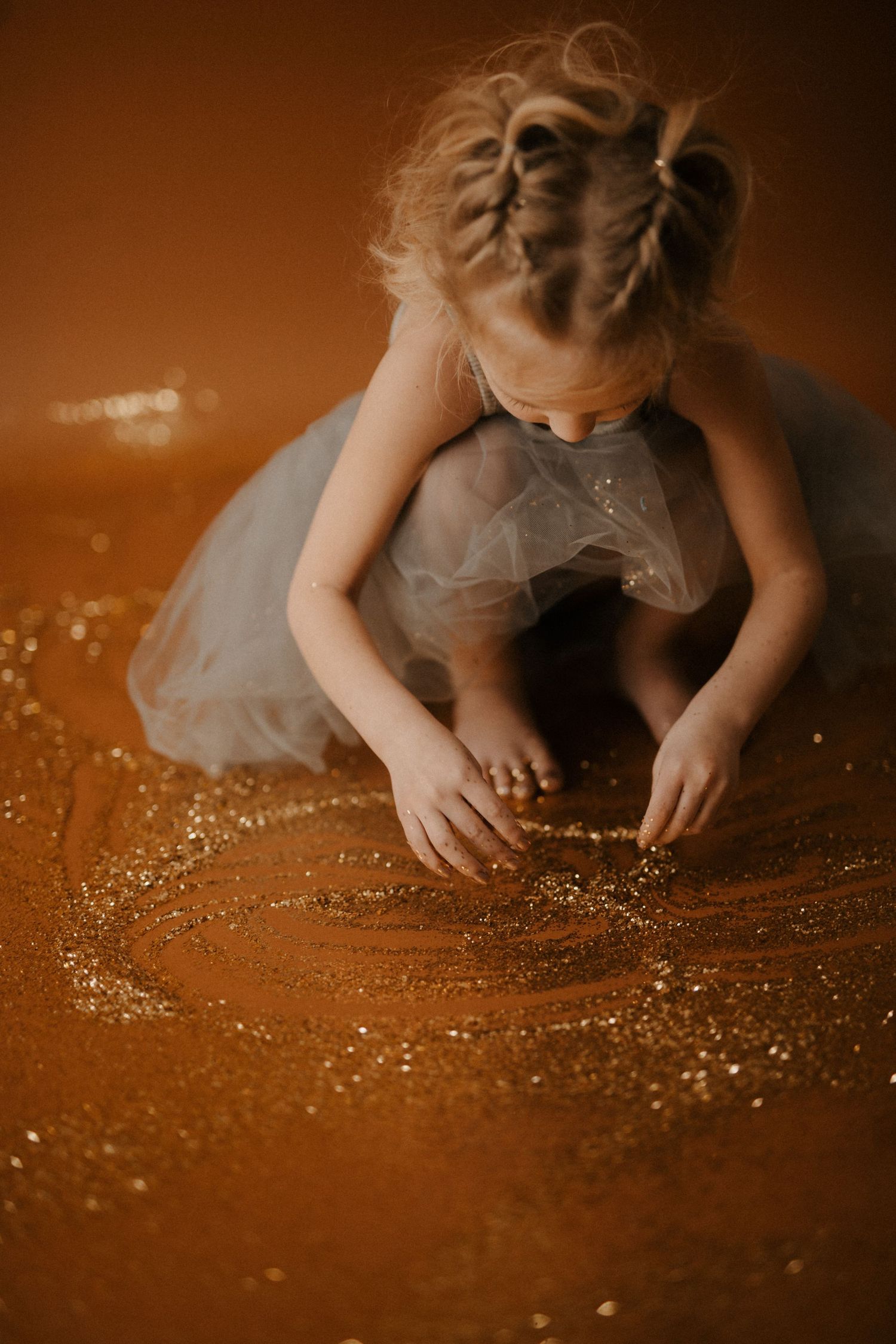A figure in a tulle dress sits on a glittery golden floor creating a dreamy, ethereal scene.