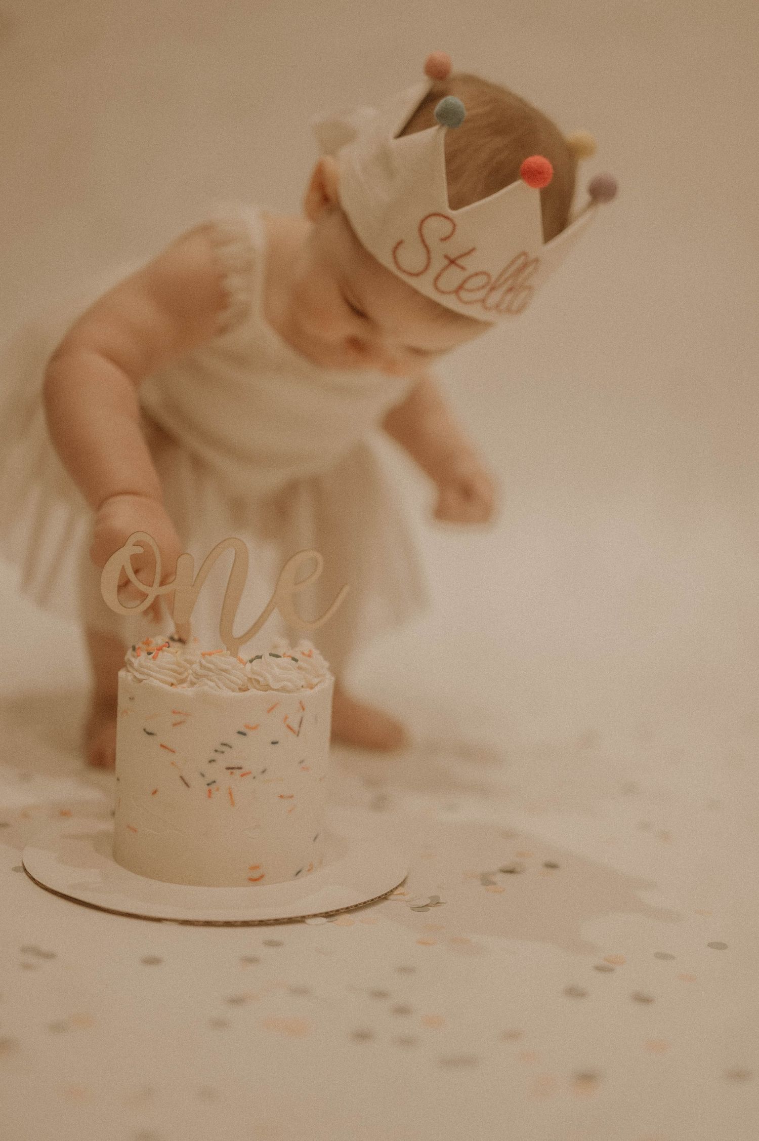 A series of four soft-focus photos showing hands decorating a white cake with confetti sprinkles on a light surface.