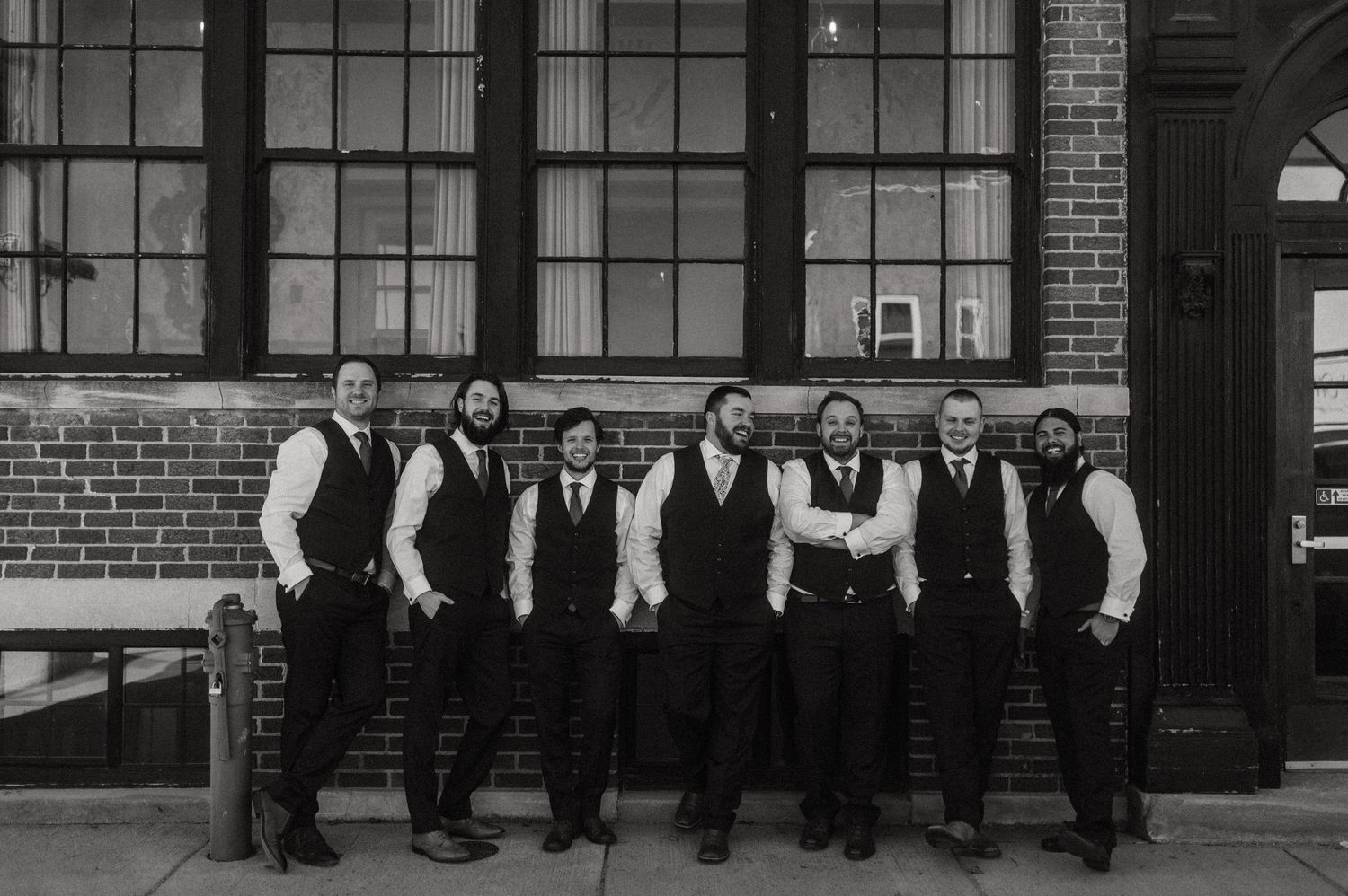 Wedding party poses in black and white photo against industrial brick building.