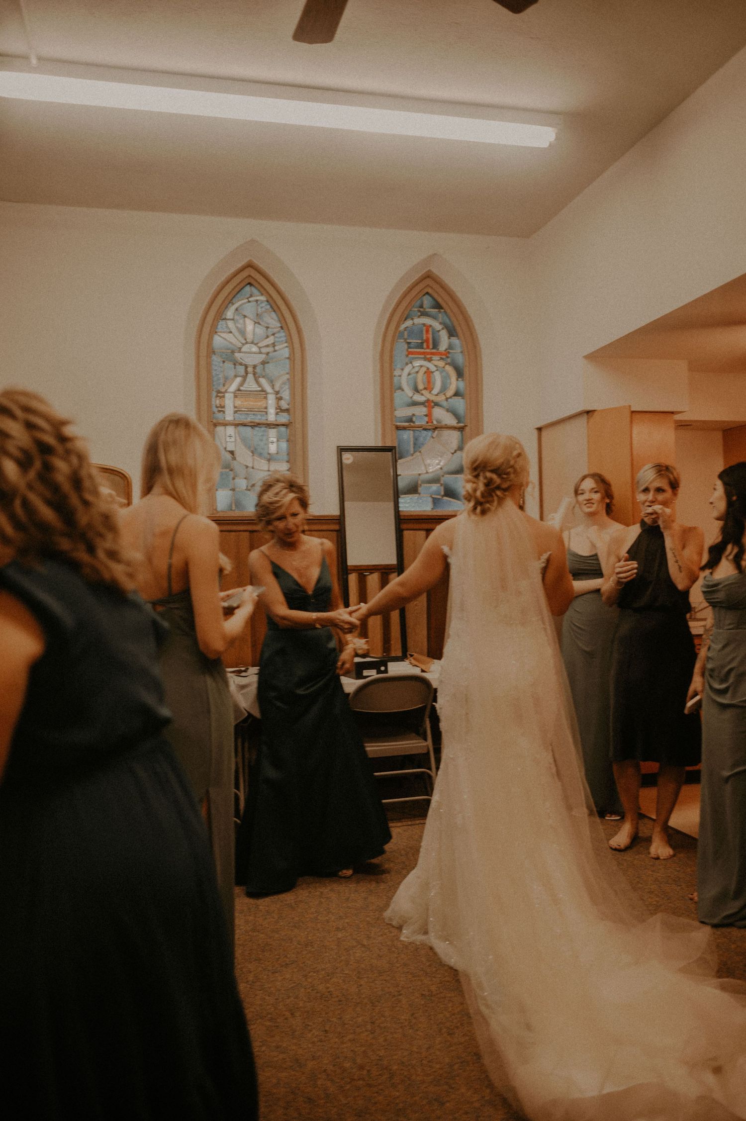 Wedding party members gather in church room with arched windows and carpeted floor.
