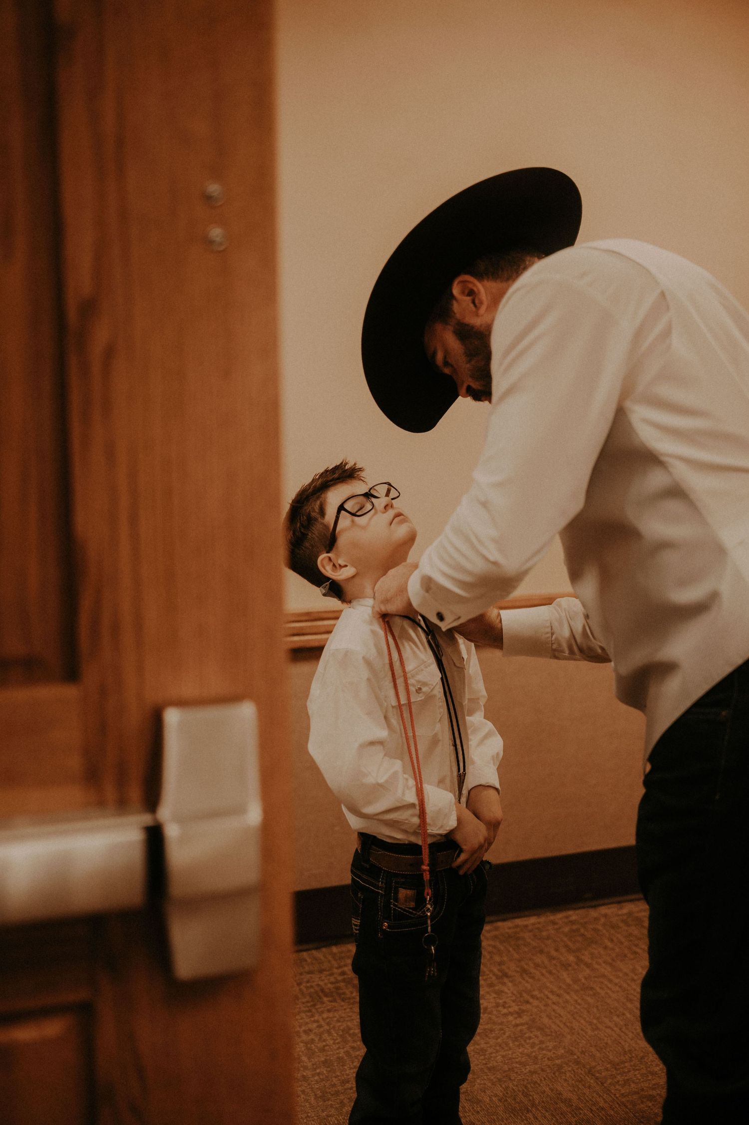 A touching interaction between an adult and child in formal attire against a warm-toned background.
