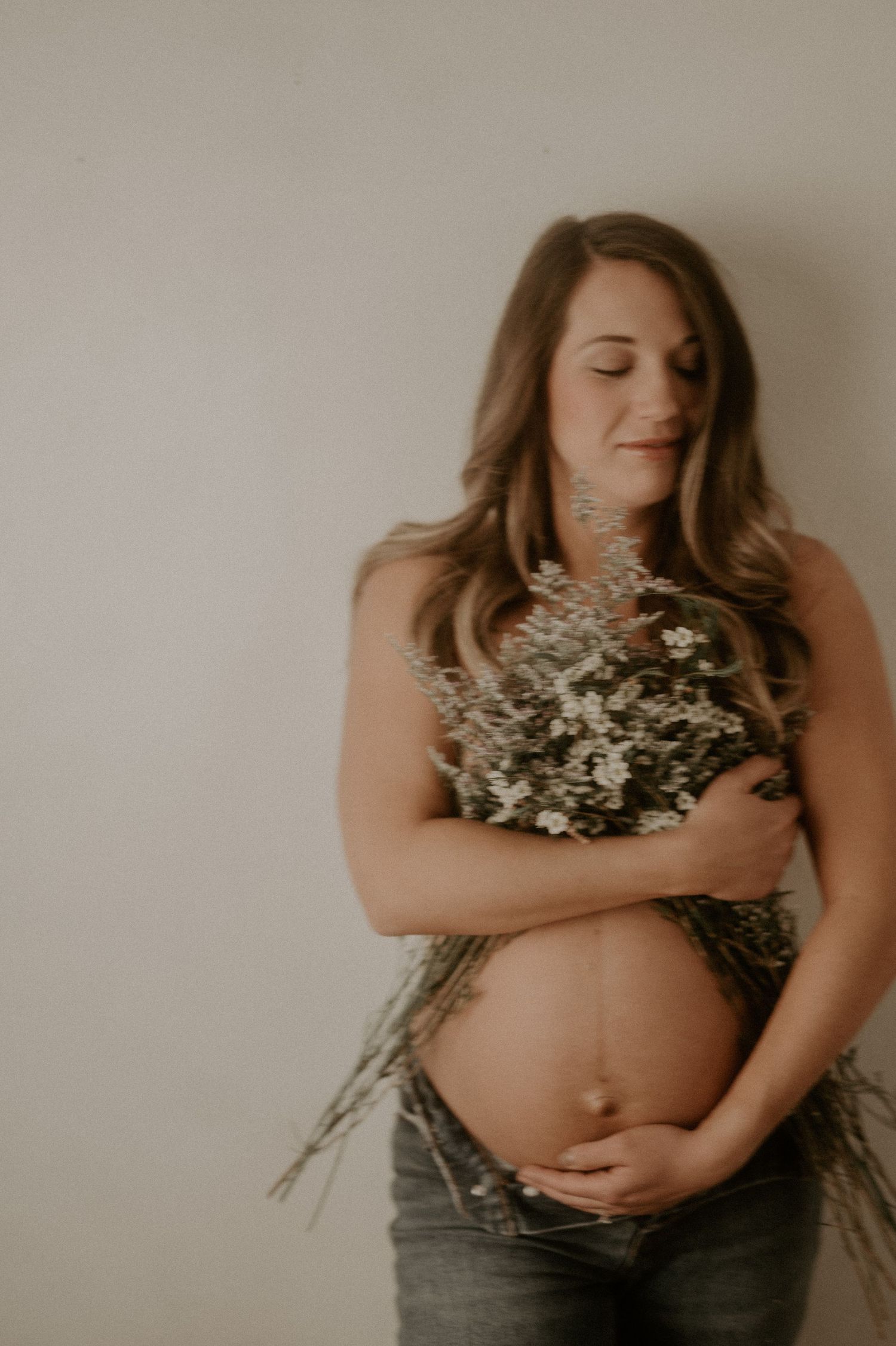 Soft-toned maternity photo with woman holding dried flowers.