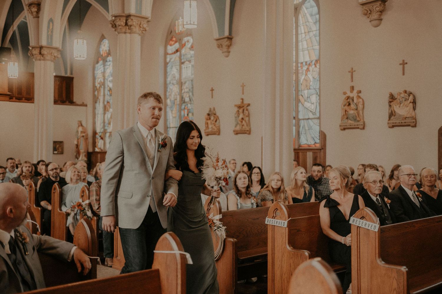 Wedding guests observe the ceremony from wooden pews in a beautifully lit church interior.