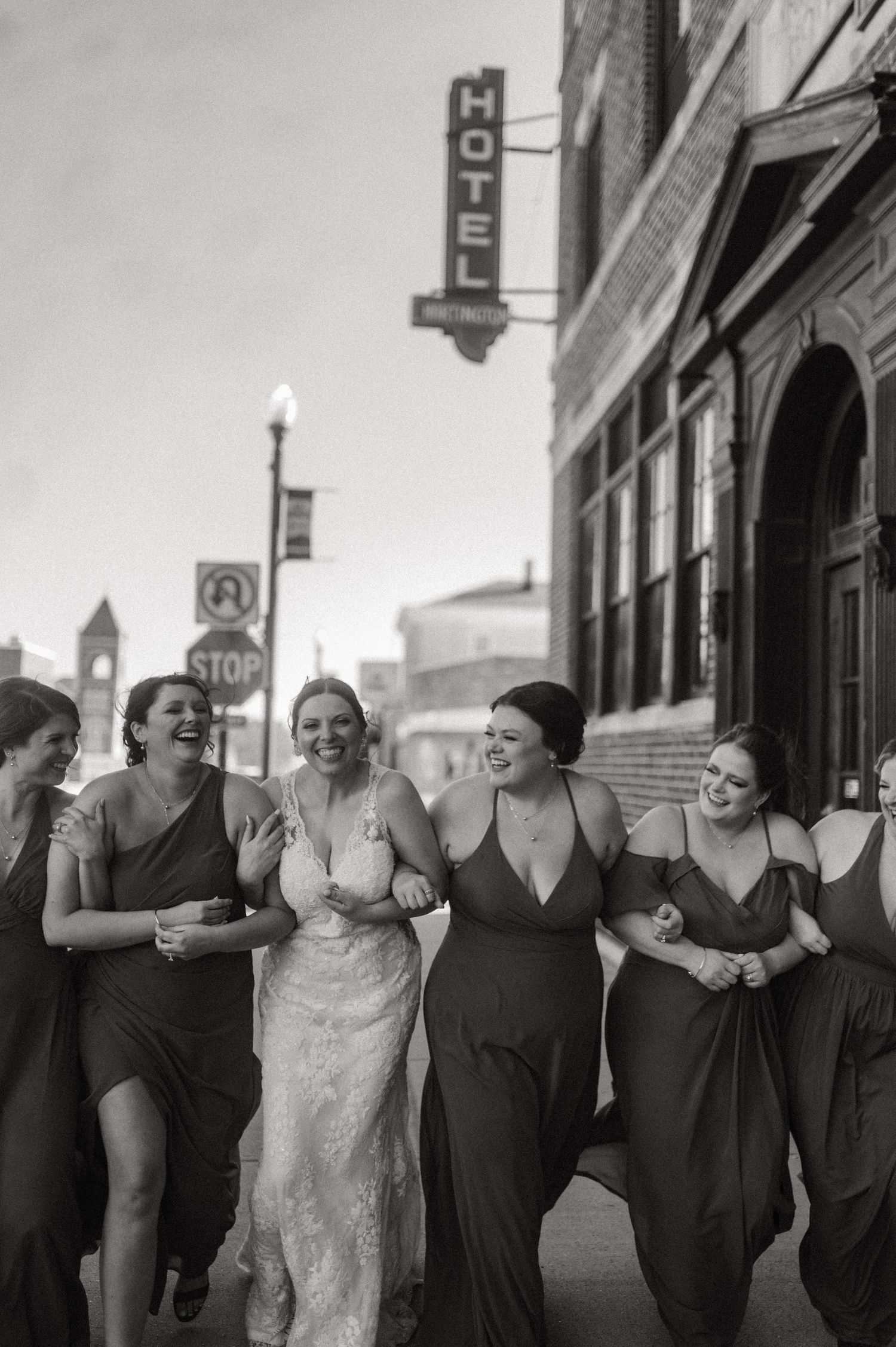 Wedding party linking arms and laughing together on urban sidewalk.