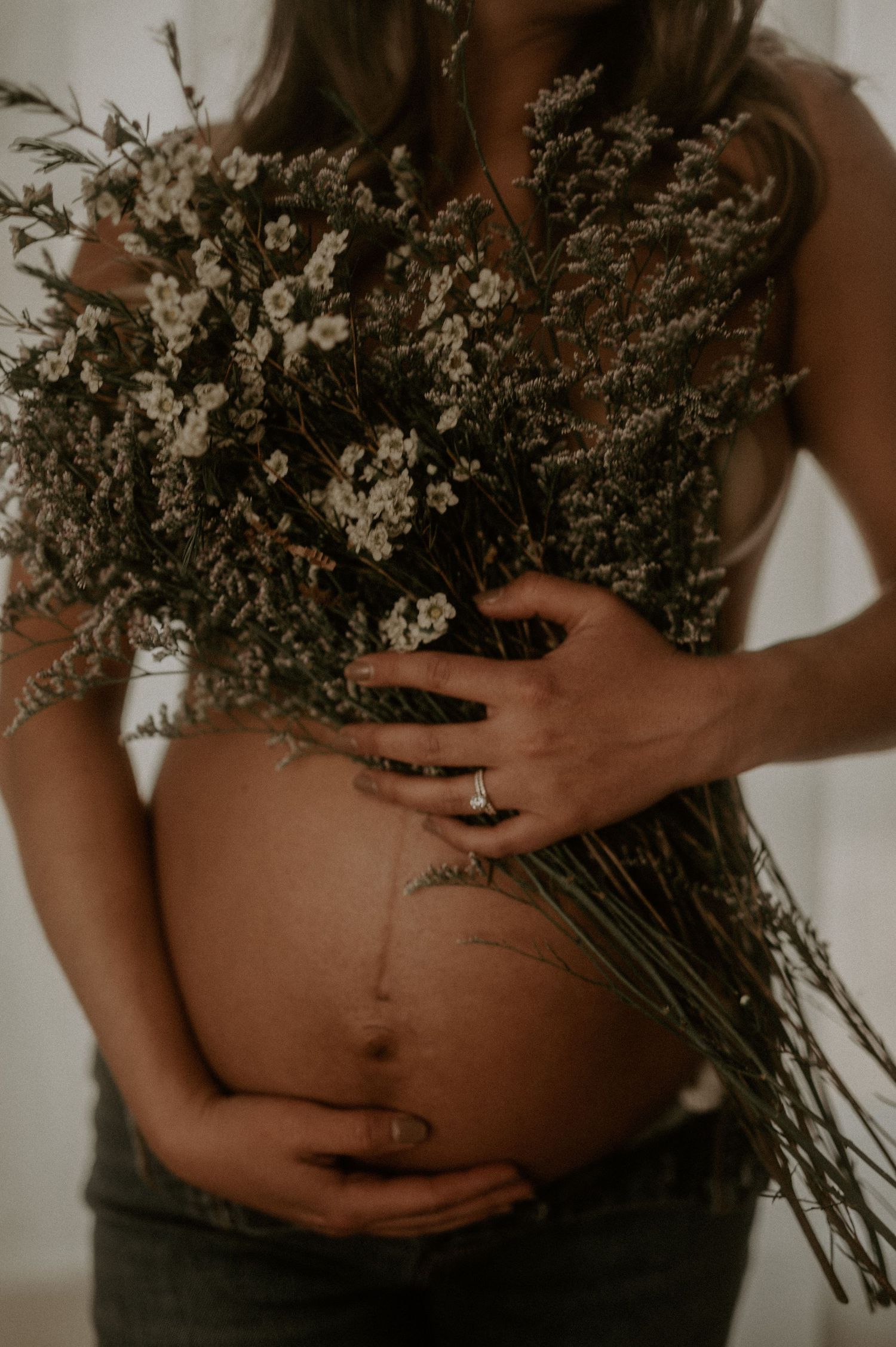 Artistic maternity photo featuring dried flower bouquet against bare belly.