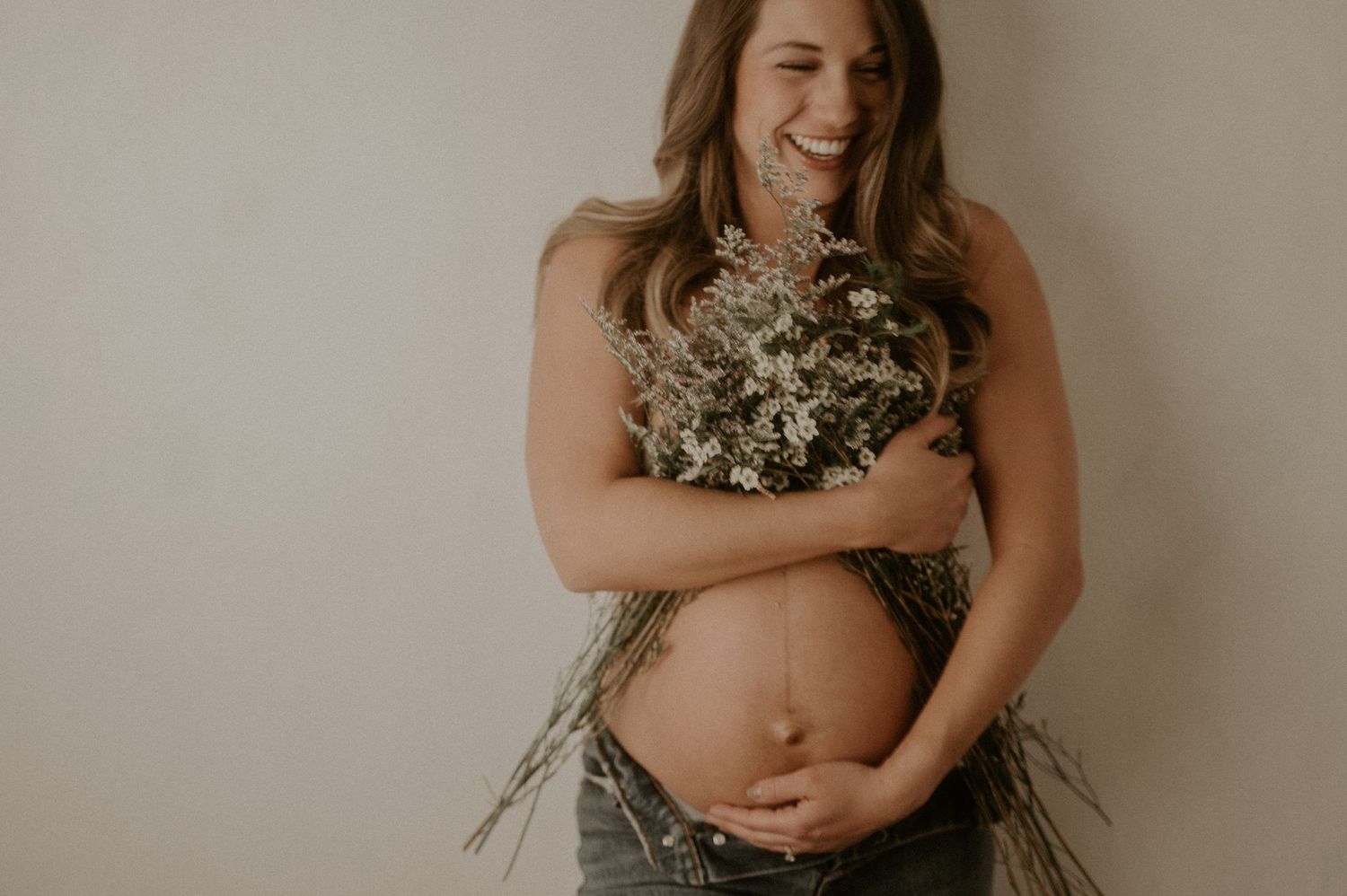 Maternity photoshoot with baby's breath flowers against neutral background.