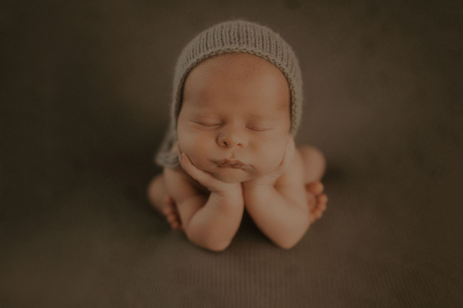 Sleeping newborn baby wearing a soft gray knit hat against a dark background.