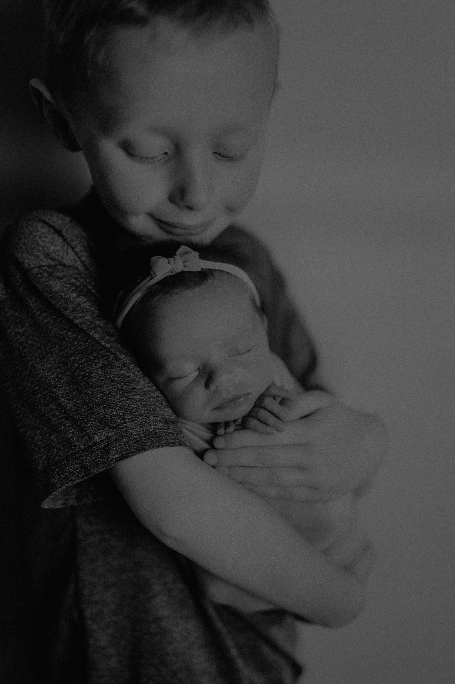 Intimate black and white photos of siblings bonding with a newborn.