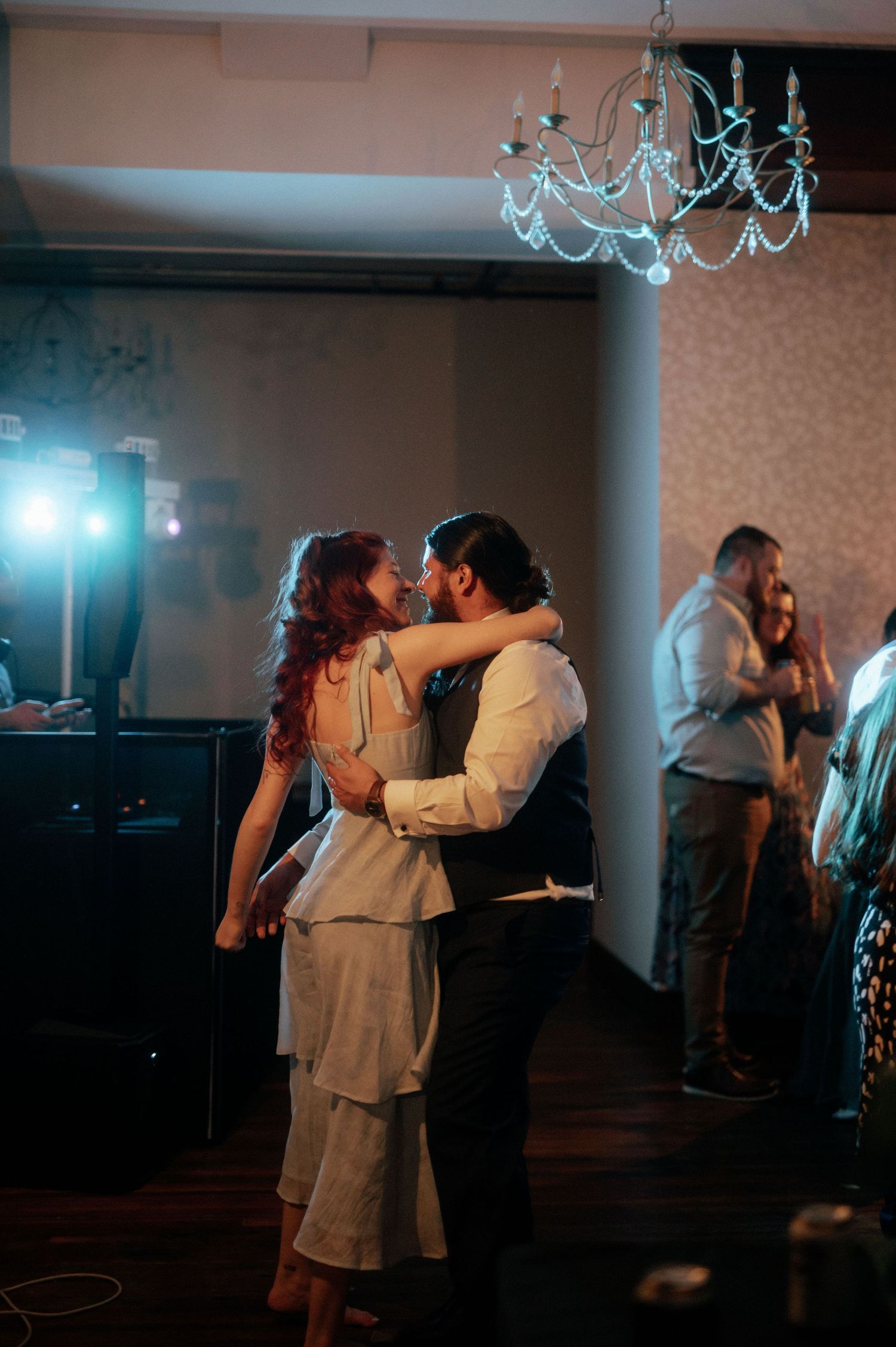 Couples slow dancing under blue lighting at an indoor wedding reception.