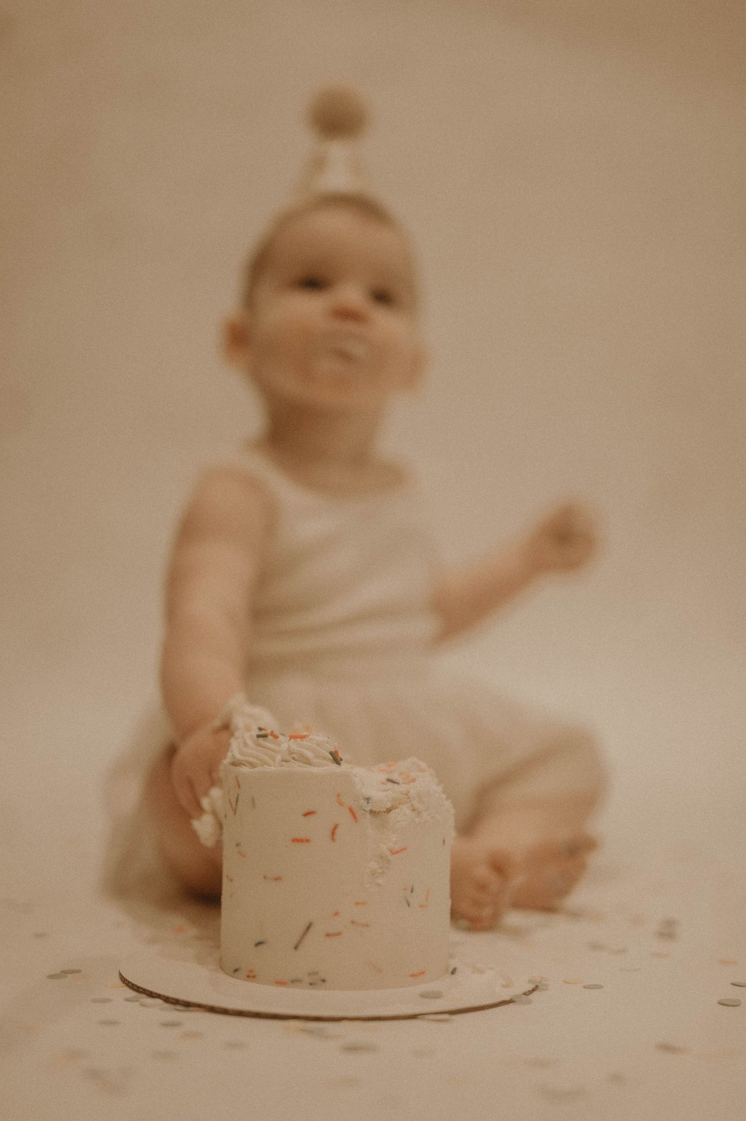 A sequence of photos showing a baby in white exploring and smashing a birthday cake in a vintage-style photoshoot.