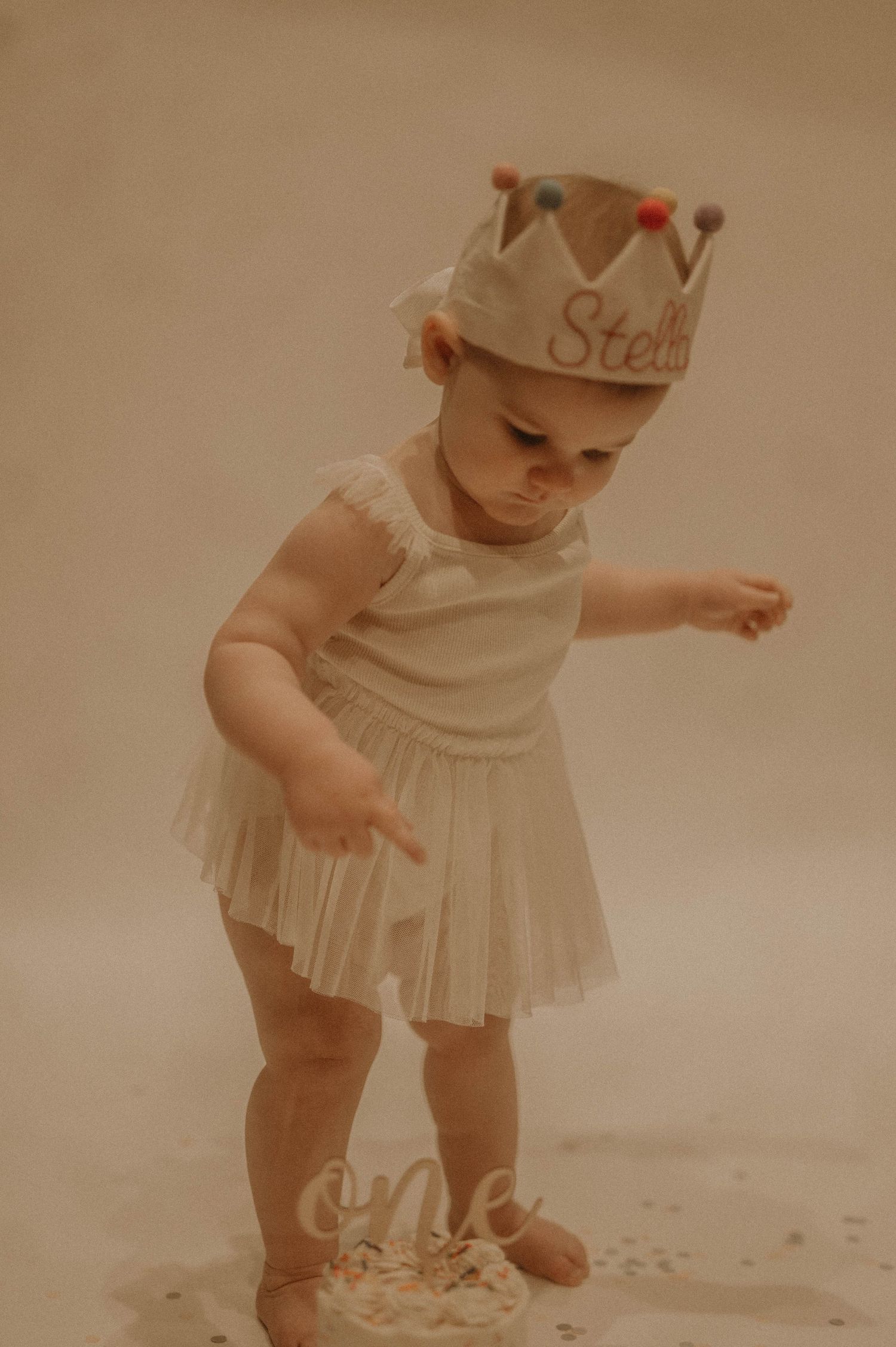 Vintage sepia photograph of a baby in a white dress exploring and playing in the sand at the beach.