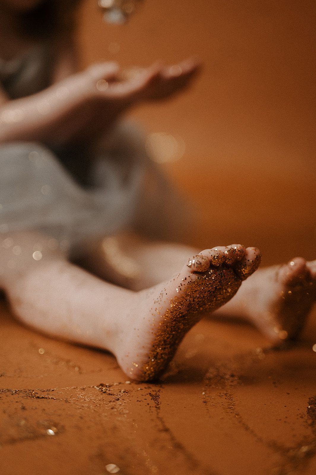 Sandy feet lying on a warm brown surface with a soft blurred background and bokeh effect.