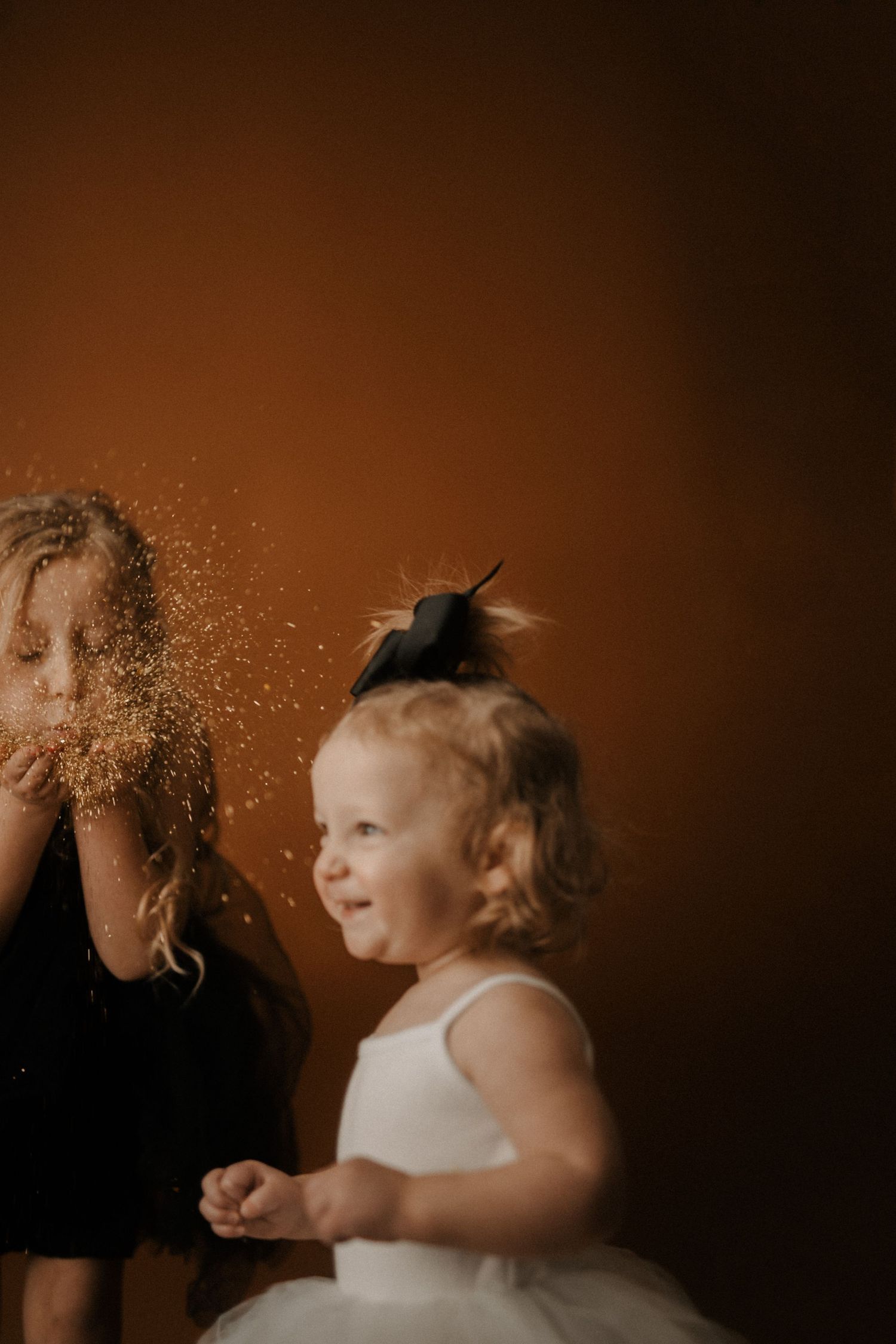 A joyful moment captured in warm tones as glitter sparkles through the air during a playful indoor photoshoot.