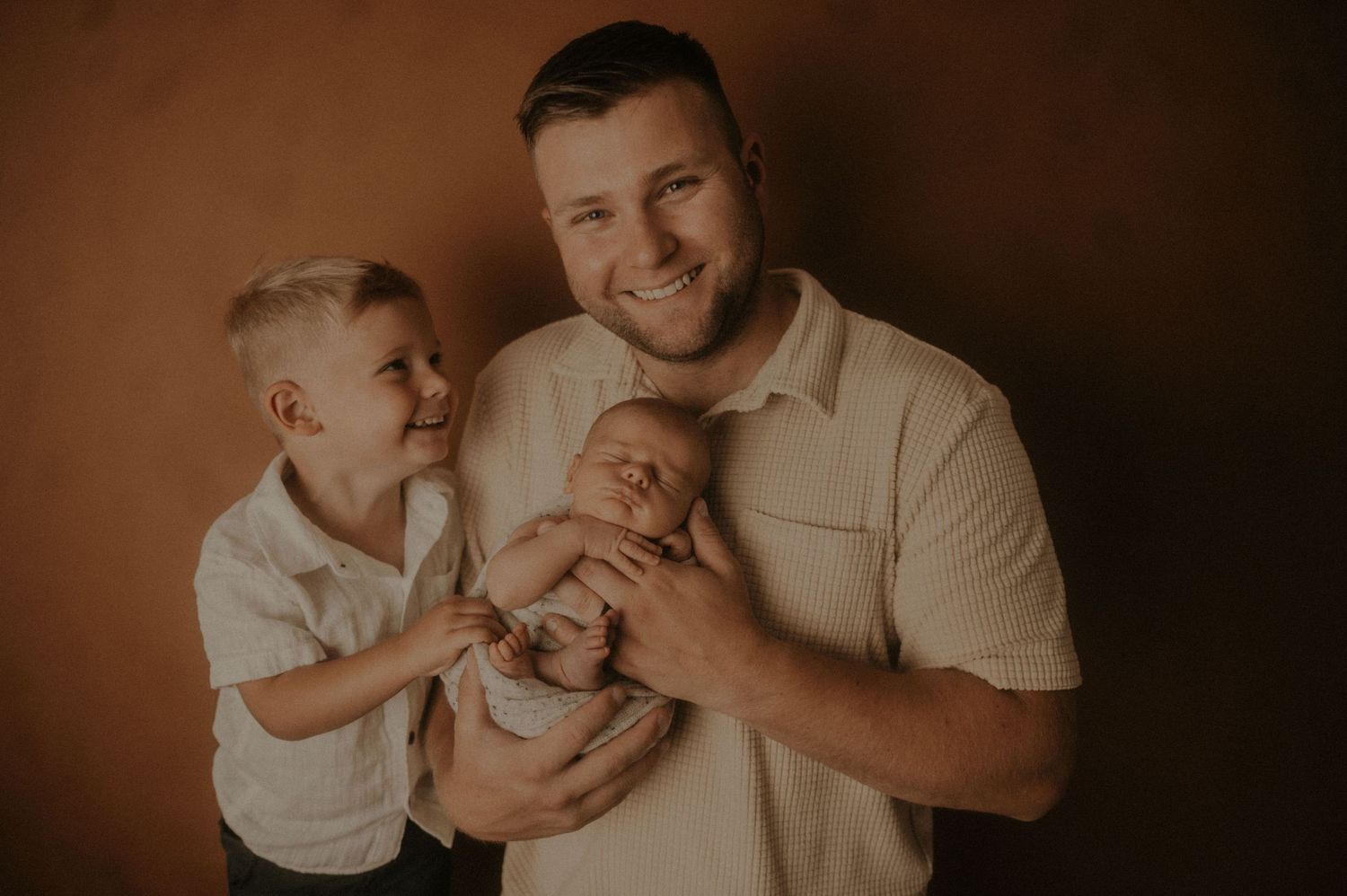 Warm toned family portrait with casual attire against dark brown background.