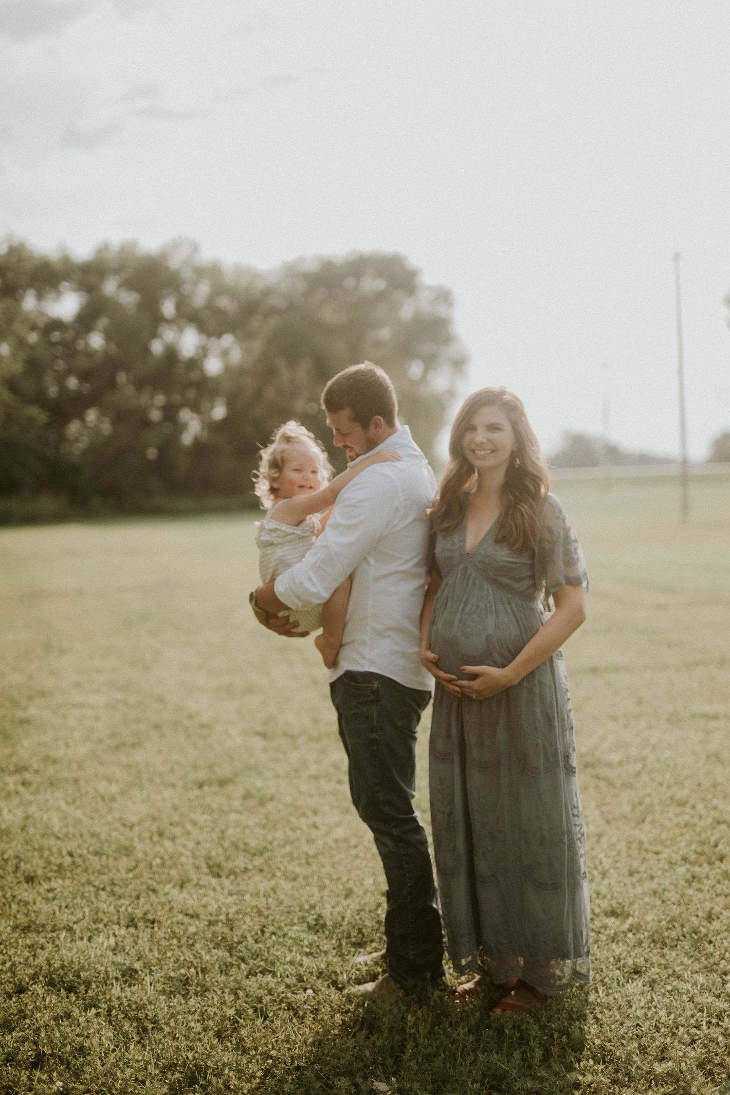 A family shares tender moments together in a sunlit field during golden hour.