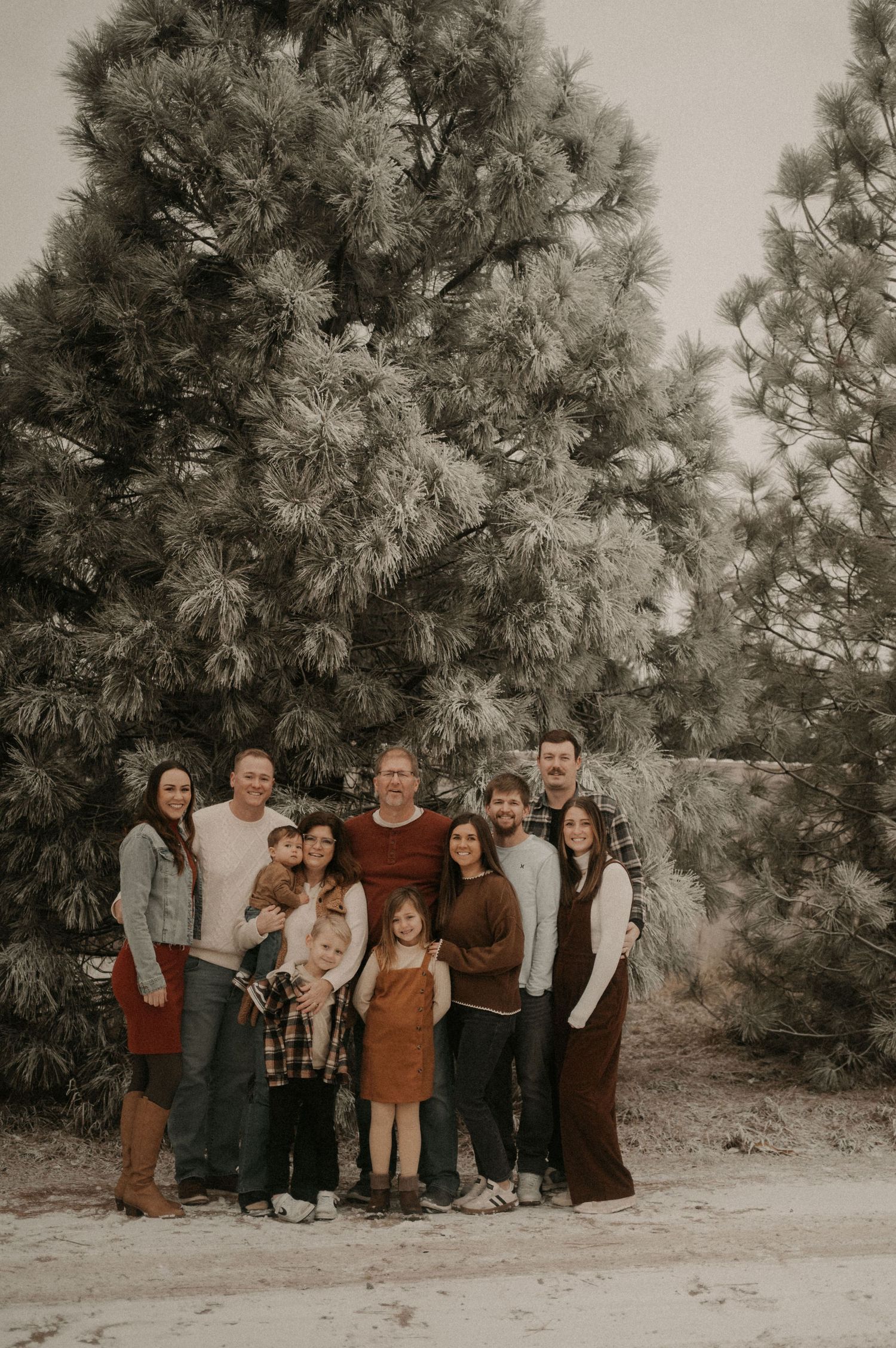A group of people pose together outdoors against a backdrop of tall pine trees in a rustic setting.