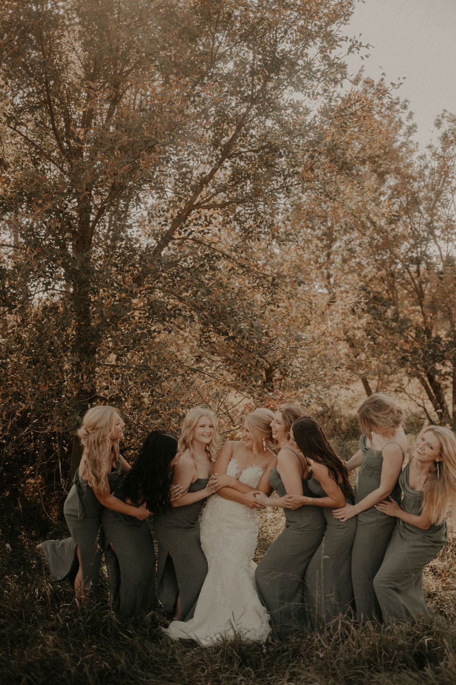 Wedding party poses in a circle against autumn trees during golden hour.
