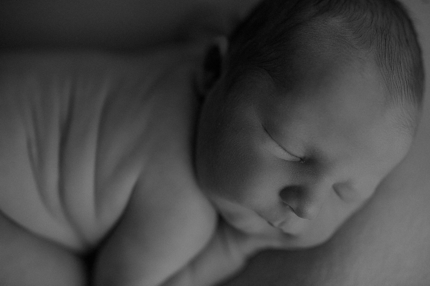 Dramatic black and white newborn portrait with moody lighting and shadows.