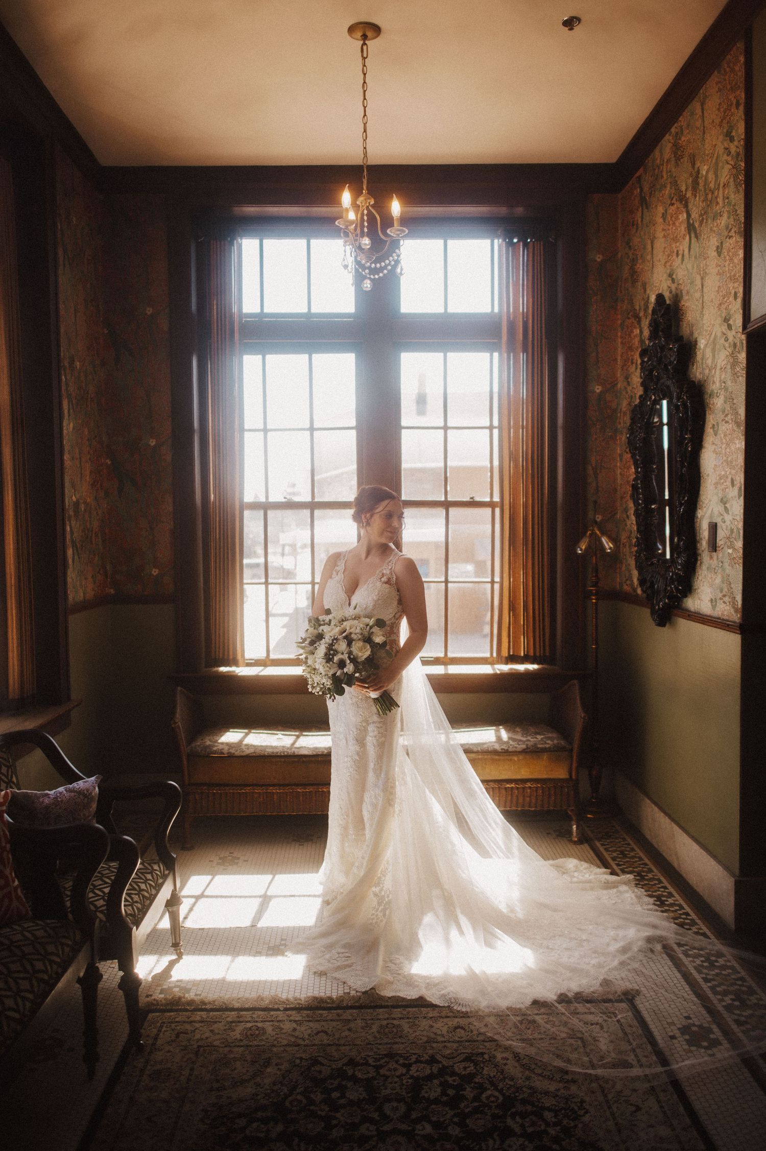 Elegant bridal portraits in a historic room with sunlight streaming through large windows.