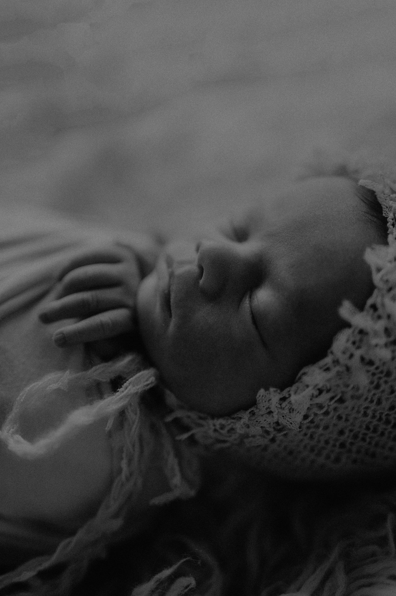 Dramatic black and white portrait of sleeping infant with lace accessories.