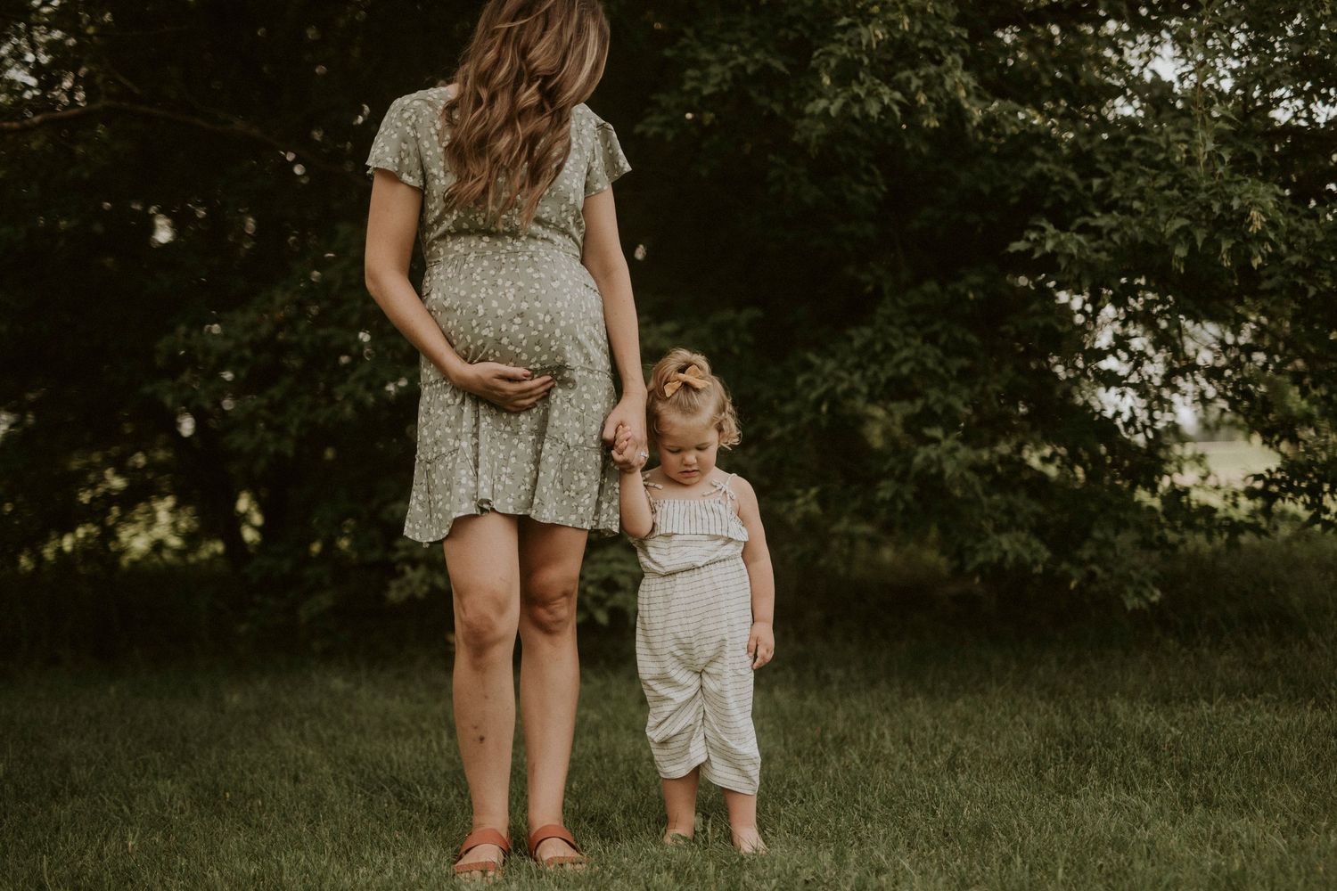 A parent and child walk hand in hand through a lush green field at sunset.