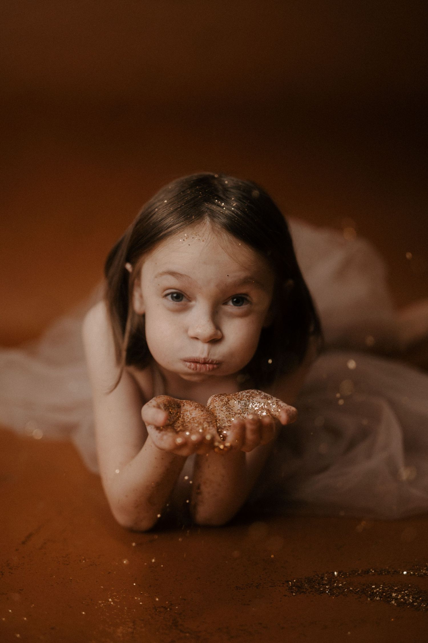 A magical portrait showing glitter being blown from cupped hands in a warm sepia-toned setting.