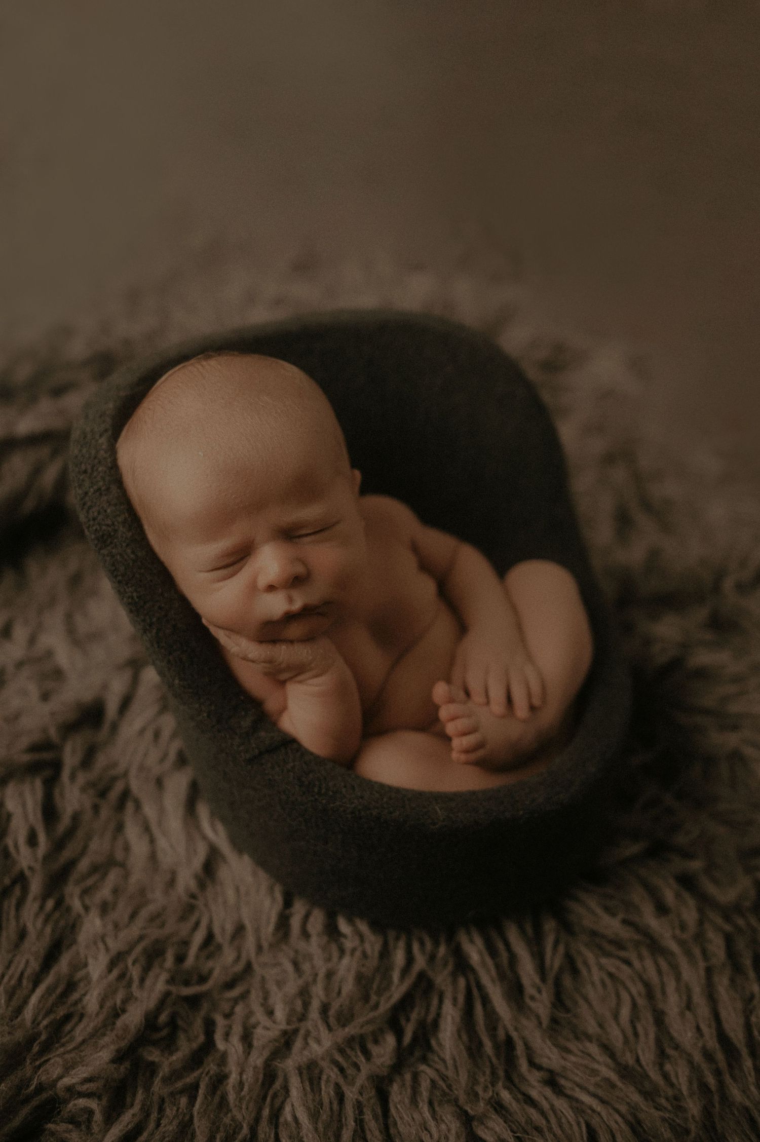 A series of artistic black and white newborn photography poses showing a sleeping baby on textured dark fabric.