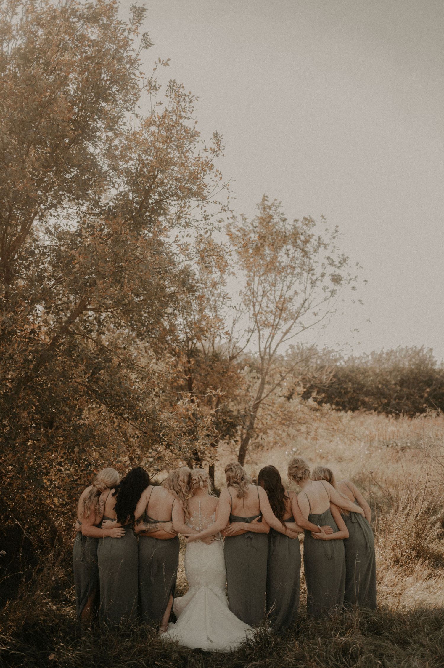 Wedding party standing together in a line against autumn trees during golden hour sunset.