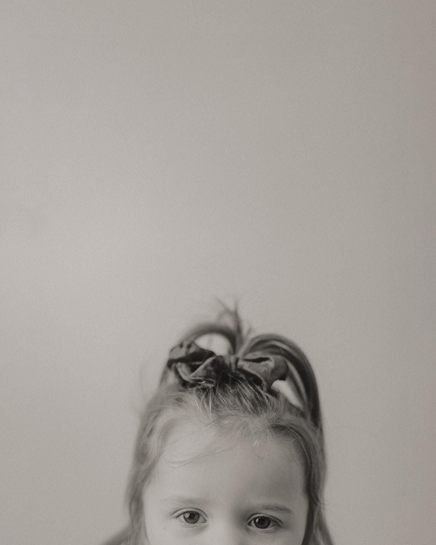 Black and white artistic portrait showing partial view of a young child against a plain background.