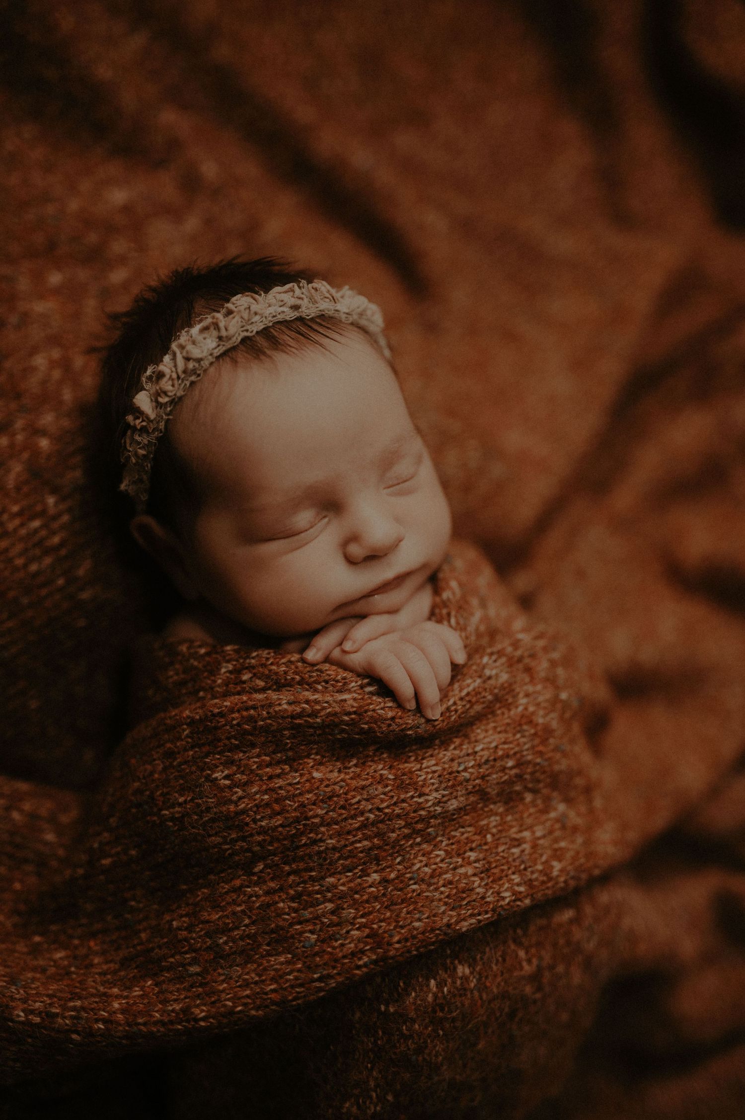 A sleeping newborn baby wrapped in a warm brown knitted blanket in a series of soft, sepia-toned photographs.