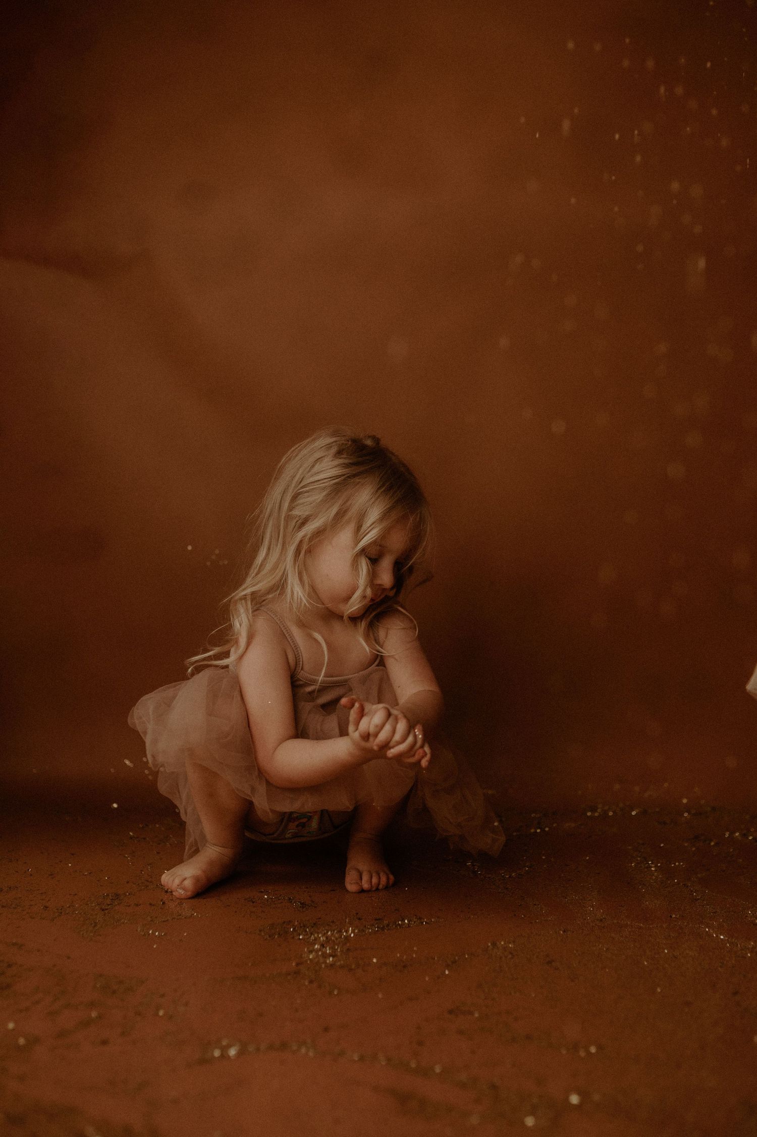 Sepia-toned artistic photo series showing a small child crawling and exploring on a dark textured floor.