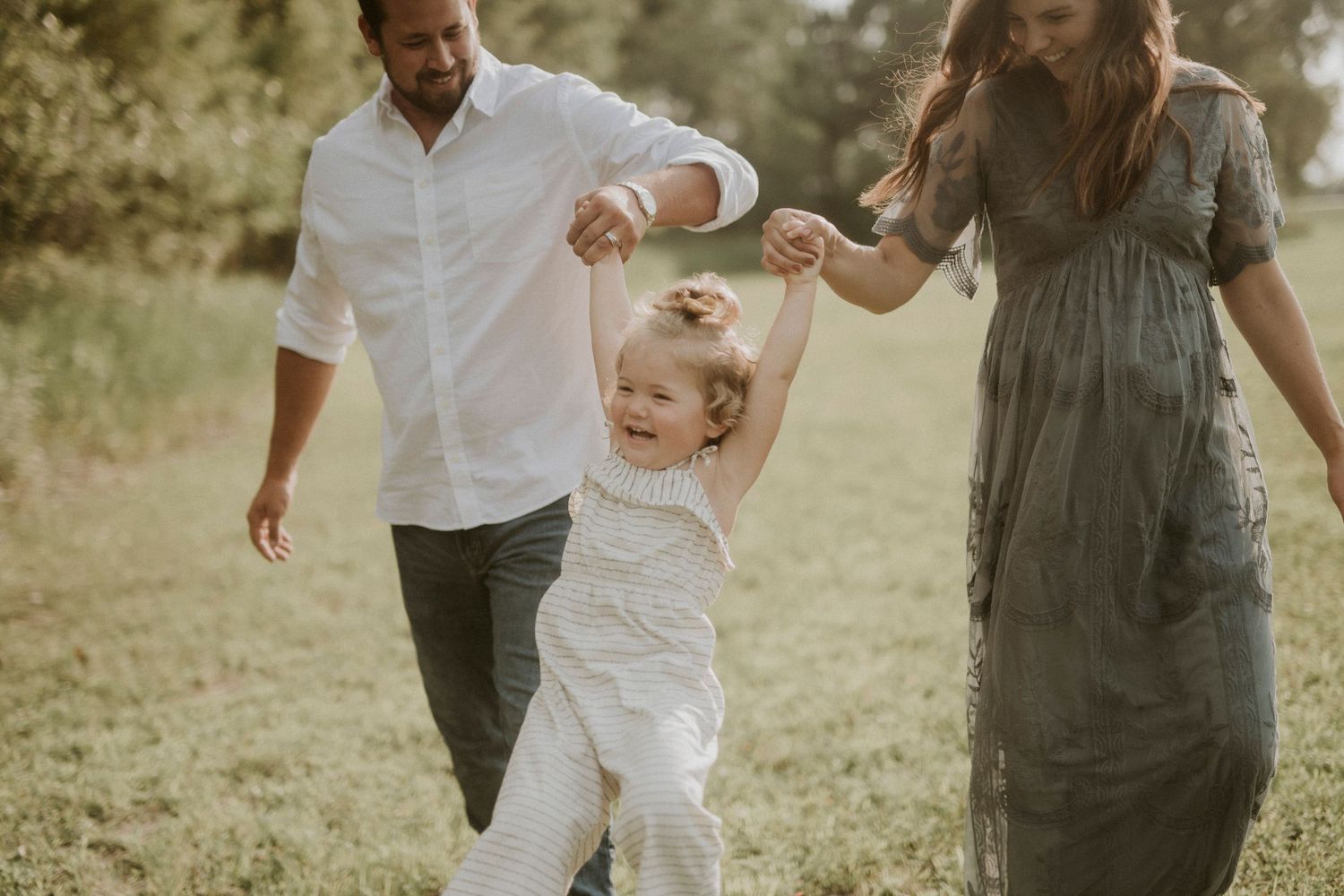 A family in white and gray outfits plays together in a sunny outdoor field during a casual photo session.