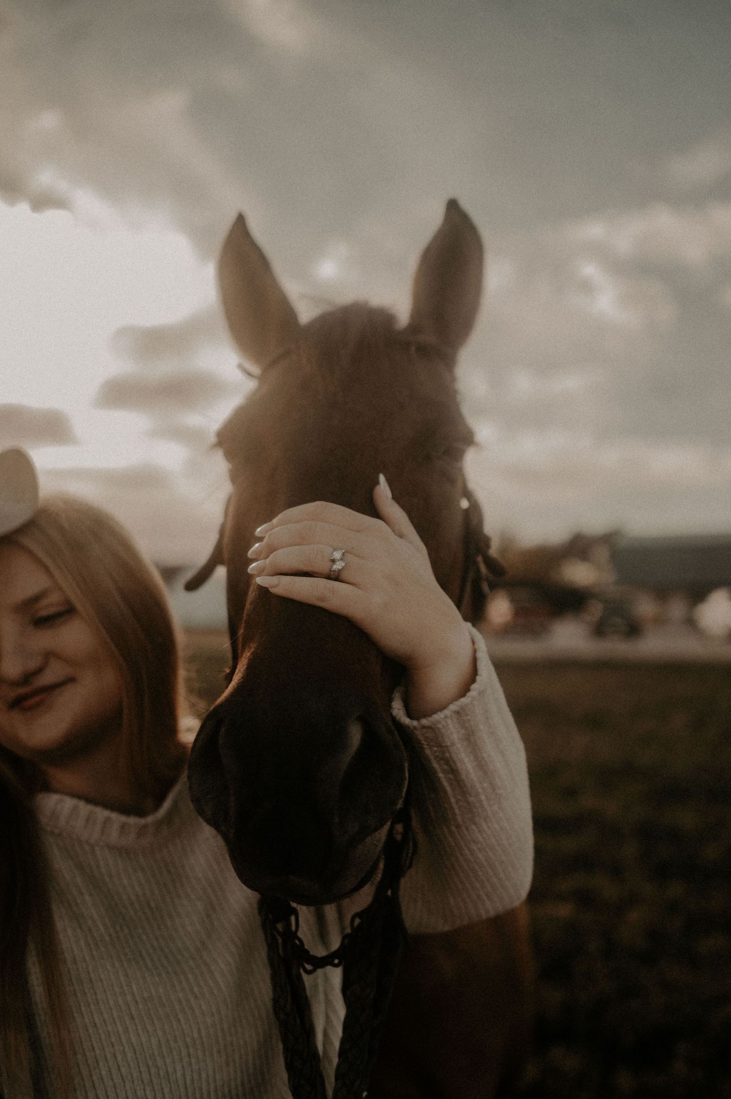 Close-up shot of a horse nuzzling against someone in a cream sweater during golden hour.