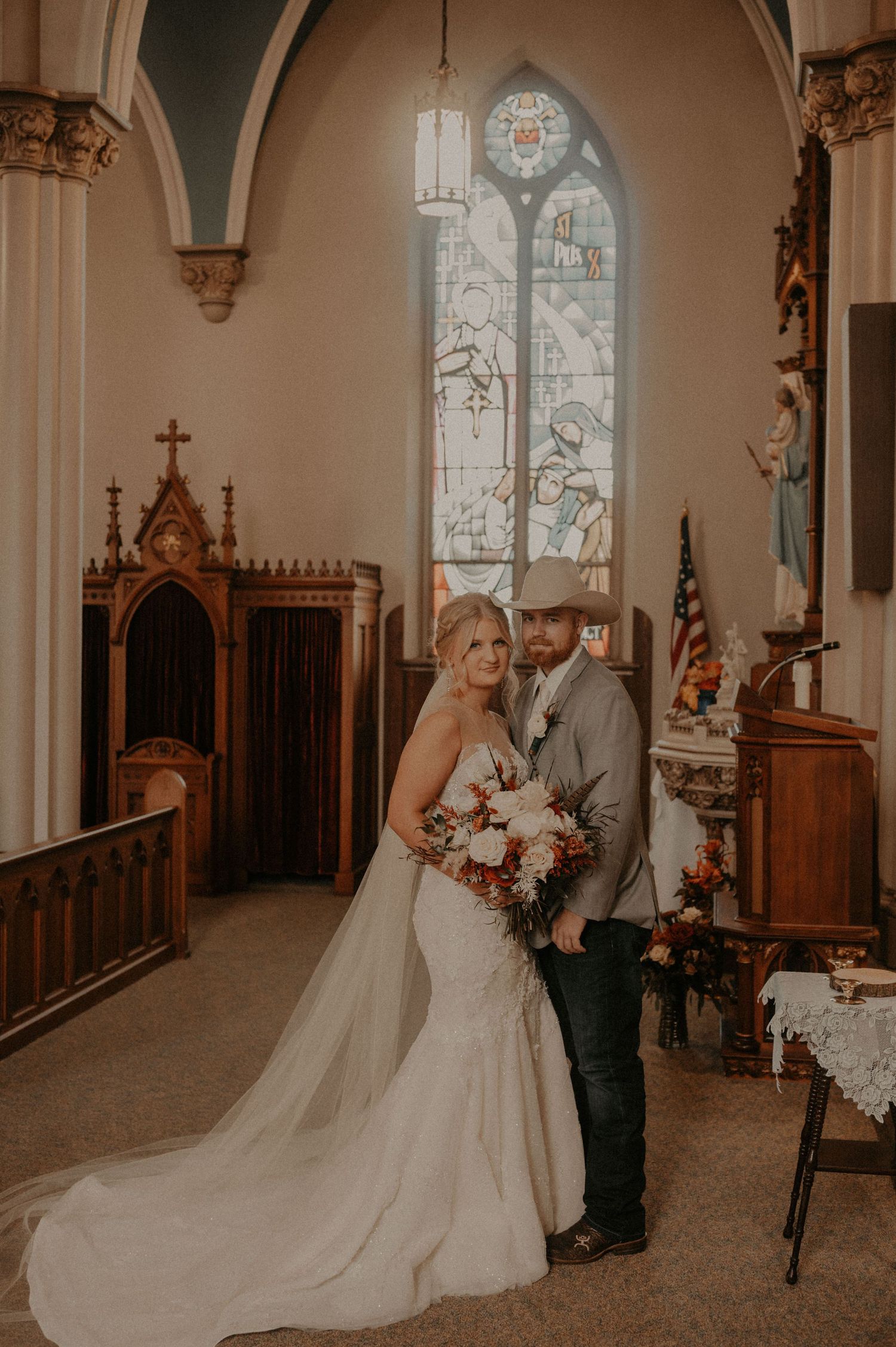 Wedding couple in western attire poses together inside historic Catholic church.