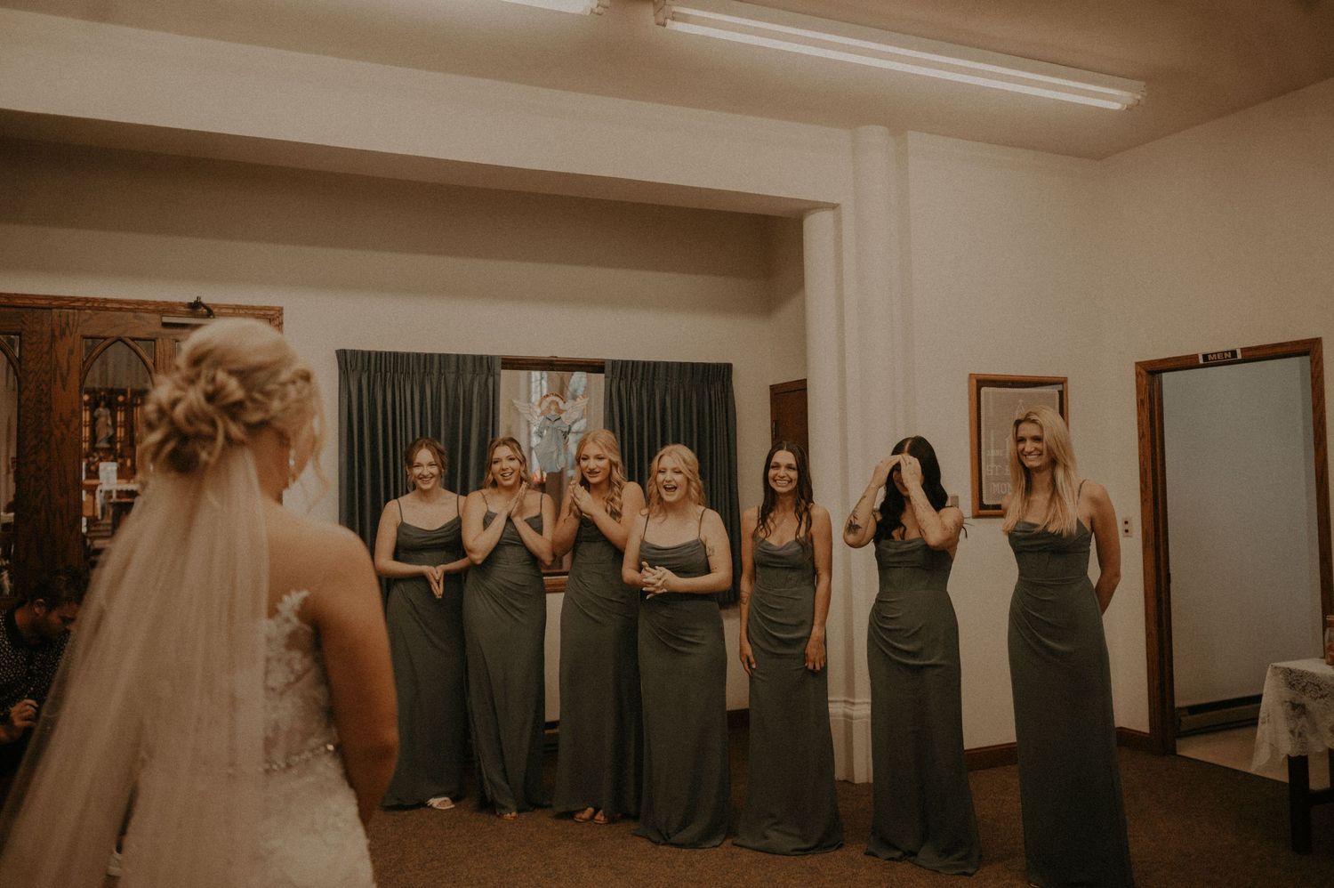 Bridesmaids in dark gray dresses stand together in an indoor venue.
