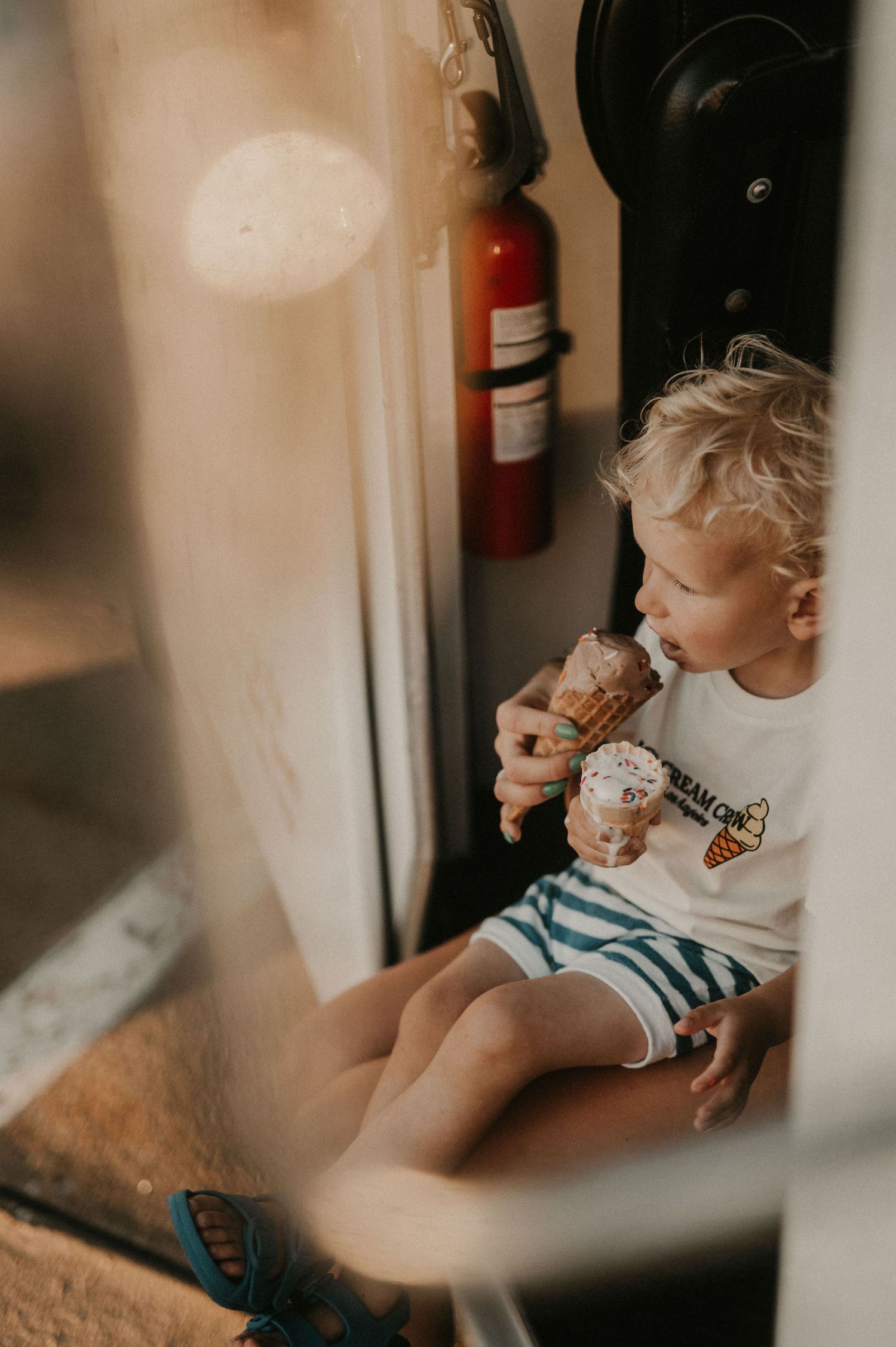 Child sitting and eating ice cream cone in casual indoor setting.