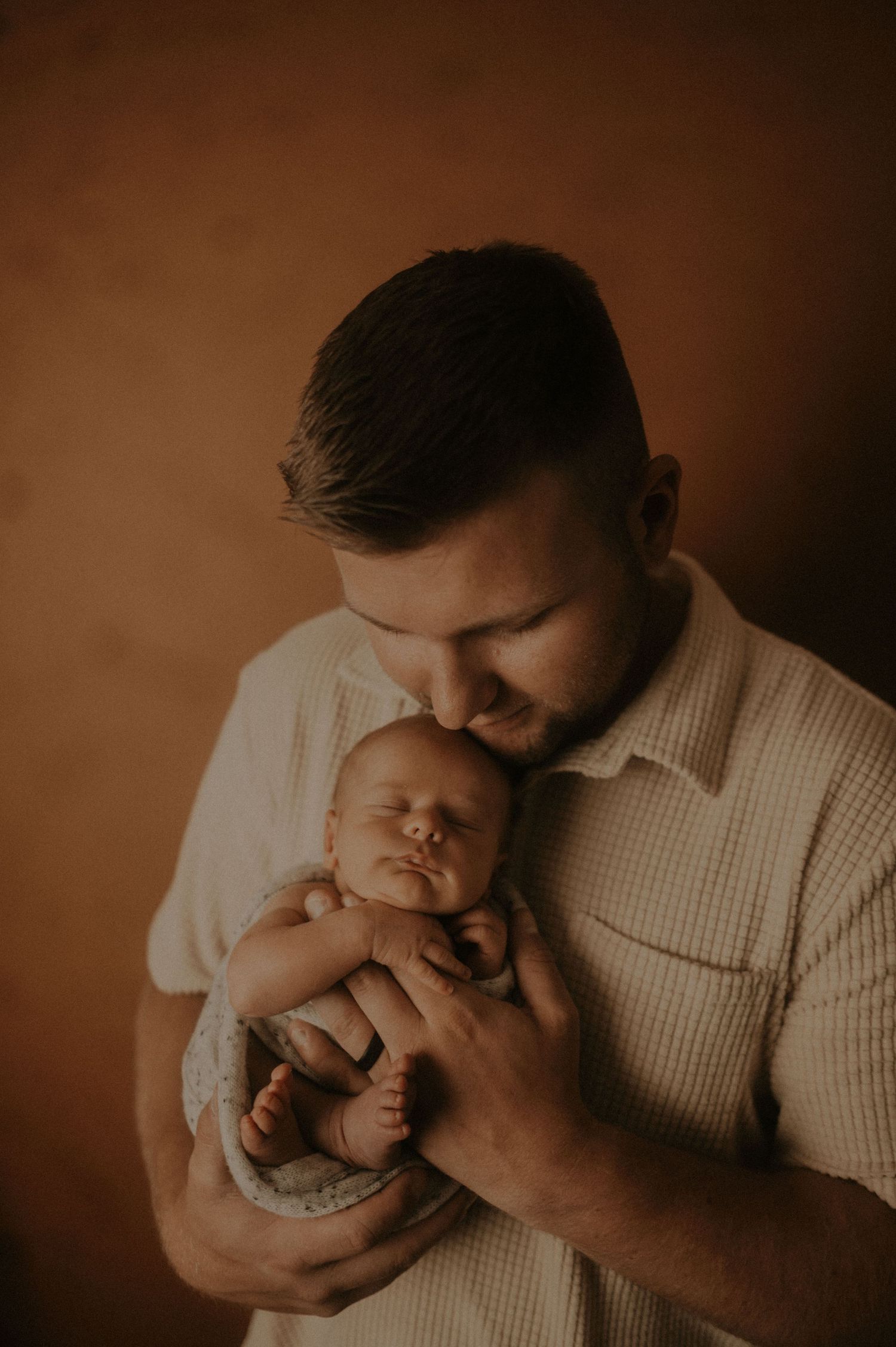Intimate sepia-toned portraits showing tender moments between parent and infant.