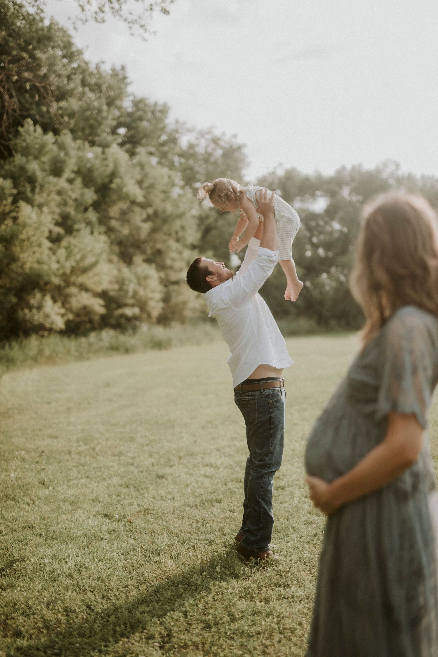 A couple playfully interacts in a sunlit meadow with dreamy, muted tones creating a romantic atmosphere.