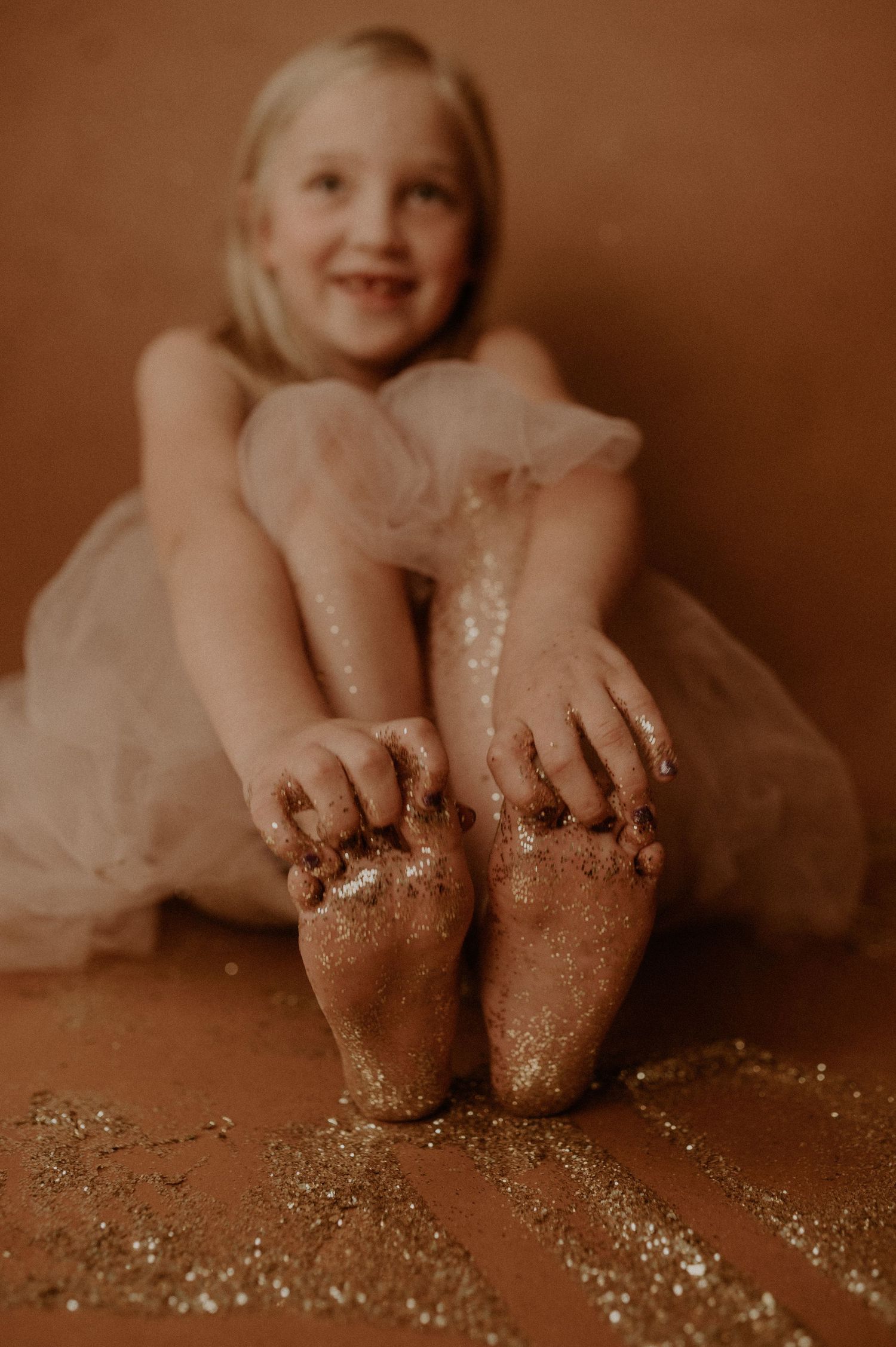 Artistic sepia-toned photo series showing small feet covered in glitter against a dark background.