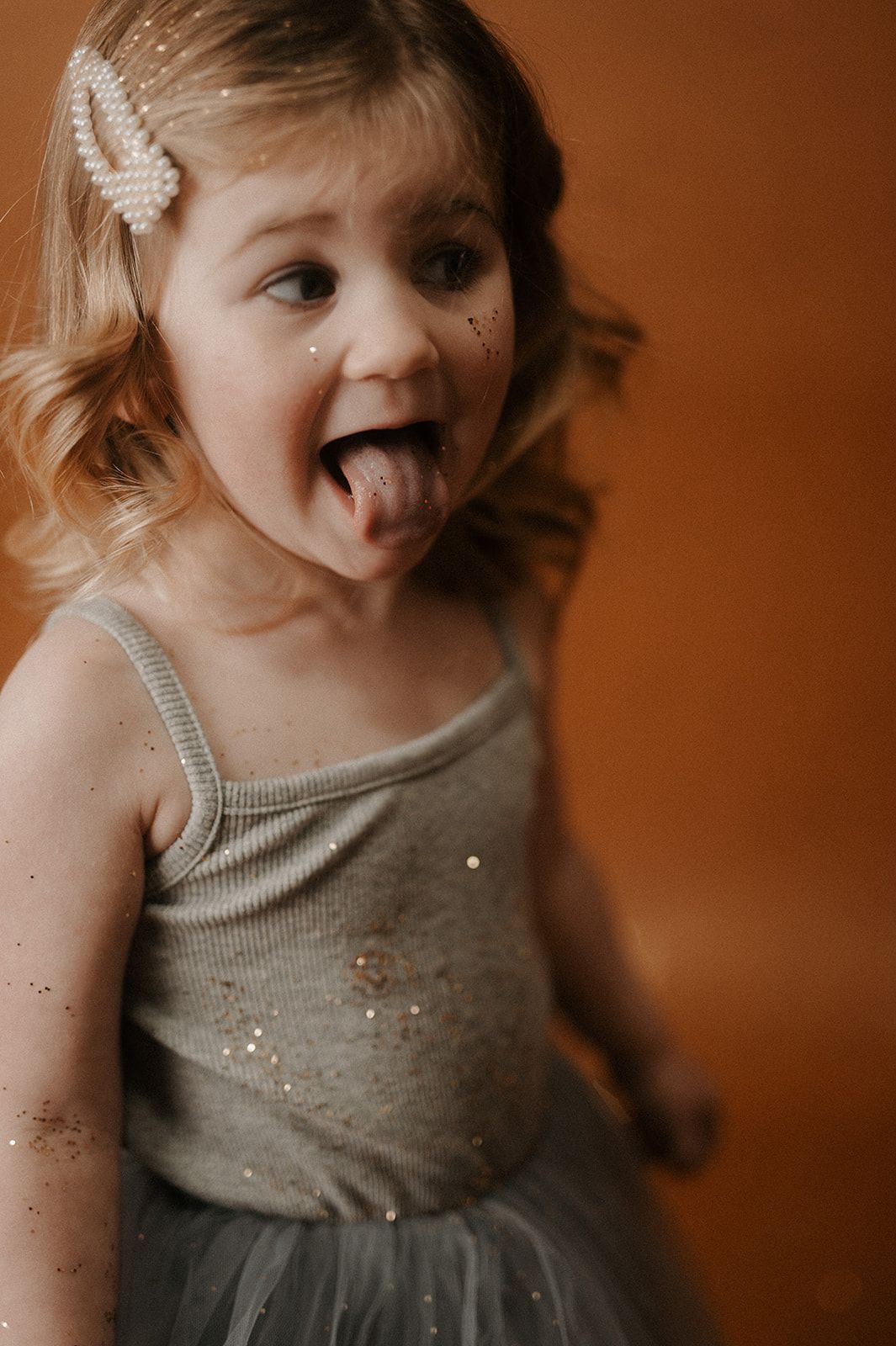 A playful series of candid moments showing a child in a gray dress against a warm brown background.